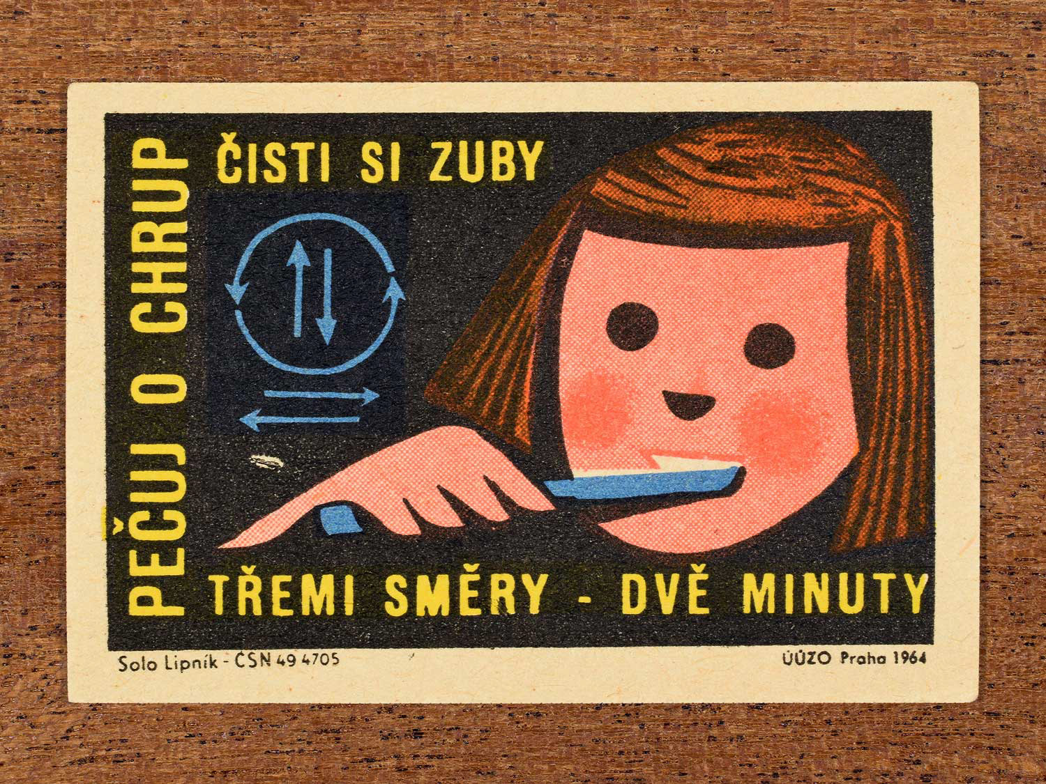 Vintage 1964 Czech matchbox label showing an illustrated child brushing its teeth with arrows in different directions, on a black background. Produced by the Solo Lipník match factory to promote nutrition advice and hygiene habits in protecting healthy teeth.