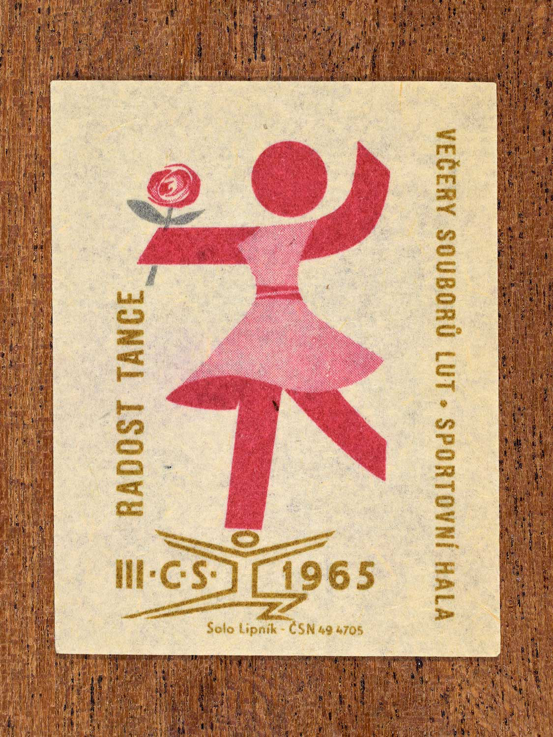 Vintage 1965 Czechoslovak matchbox label showing a stylised dancer holding a flower. In pink and gold colours. Produced by the Solo Lipník match factory to promote joyful social dance.