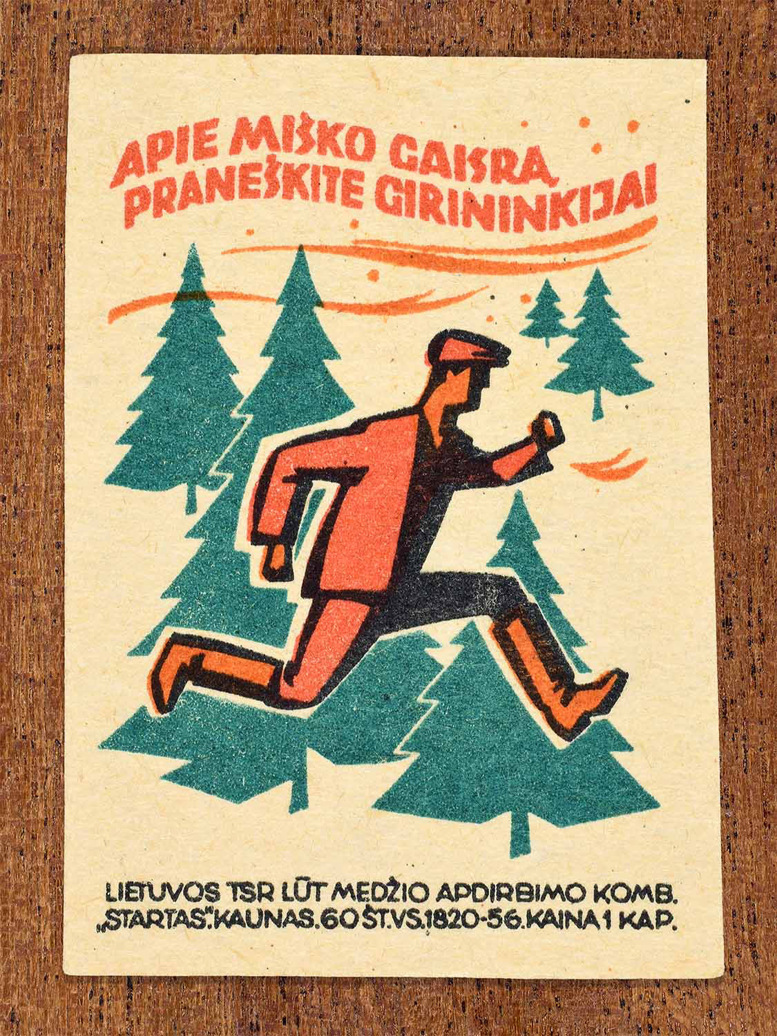 Vintage 1964 Lithuanian matchbox label showing a man running through a forest. In black, green and orange colours. Produced by the Startas match factory to promote reporting forest fires.