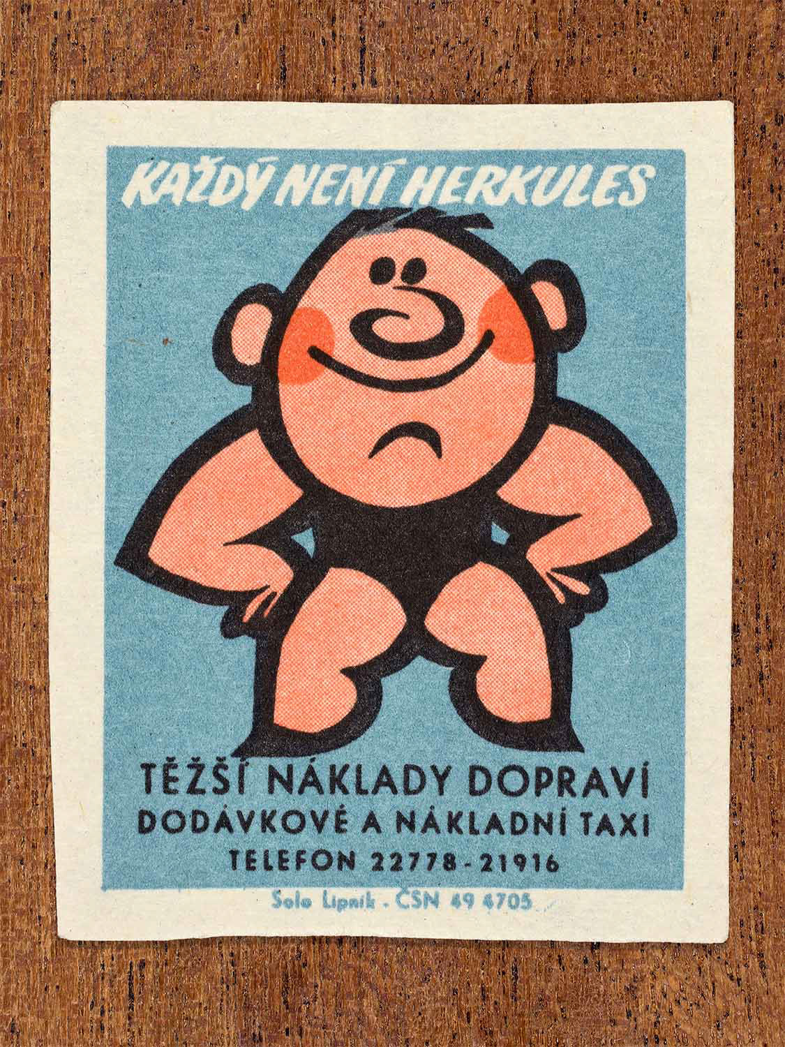 Vintage 1967 Czech matchbox label showing a smiling cartoon strongman, on a blue background. Produced by the Solo Lipník match factory to promote municipal cargo transport services.