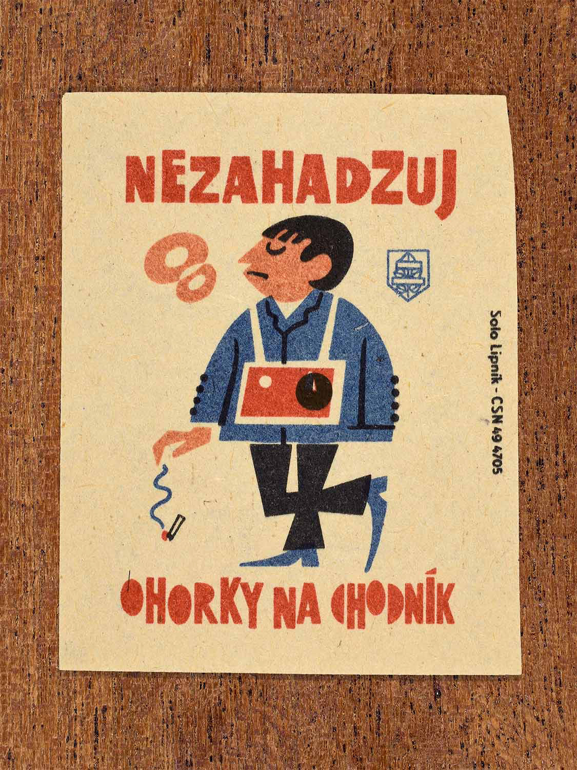 Vintage 1964 Czech matchbox label showing a man dropping a cigarette butt onto a pavement, in blue, red and black colours. Produced by the Solo Lipník match factory to discourage littering cigarette ends in public spaces.
