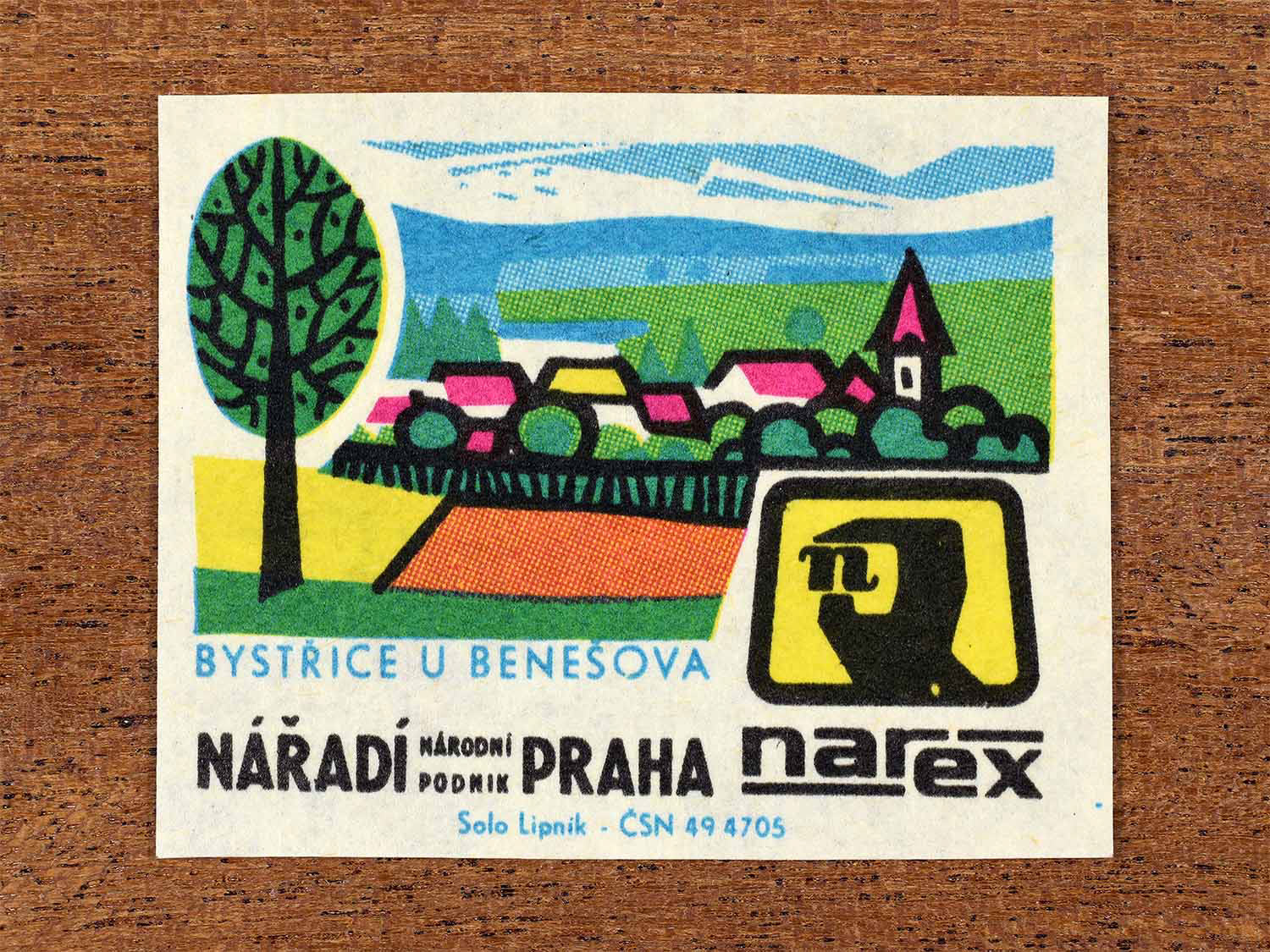 Vintage 1967 Czech matchbox label showing a stylised rural townscape with houses, fields, and a church in multiple bright colours. Produced by the Solo Lipník match factory to promote the Bystřice and Narex, the national tool enterprise in Czechoslovakia.