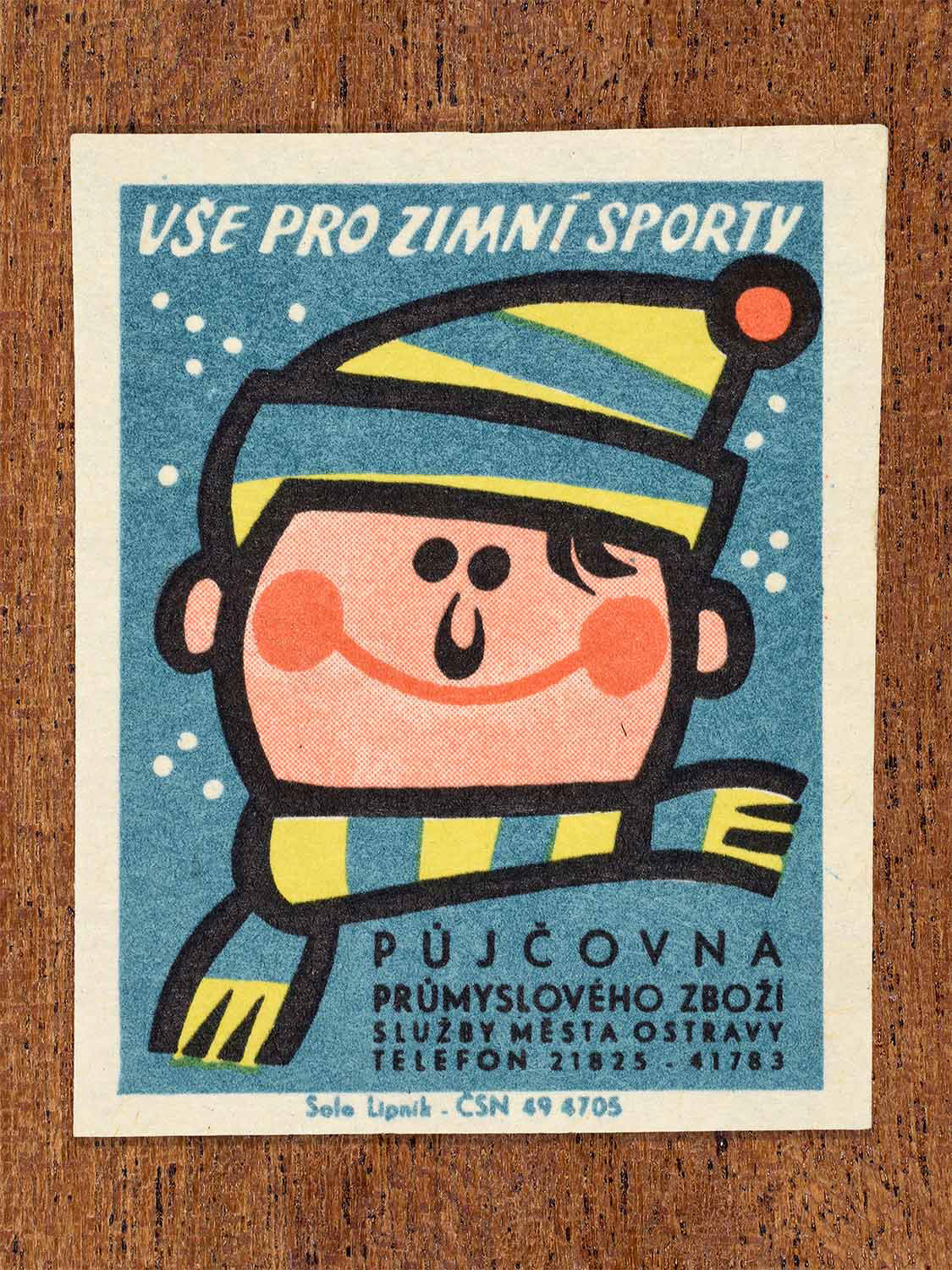 Vintage 1967 Czech matchbox label showing a smiling cartoon child in winter hat and scarf, on a blue background. Produced by the Solo Lipník match factory to advertise municipal winter sports equipment rental services.