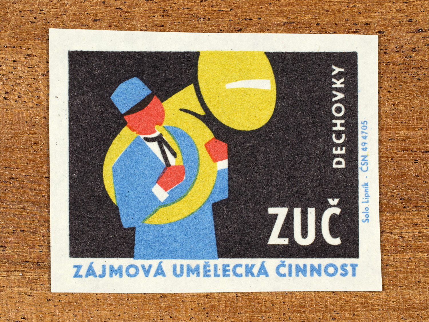 Vintage 1969 Czech matchbox label showing a stylised figure playing a sousaphone wind instrument, in blue, red, yellow and black colours. Produced by the Solo Lipník match factory to promote state-organised art groups in Czechoslovakia.