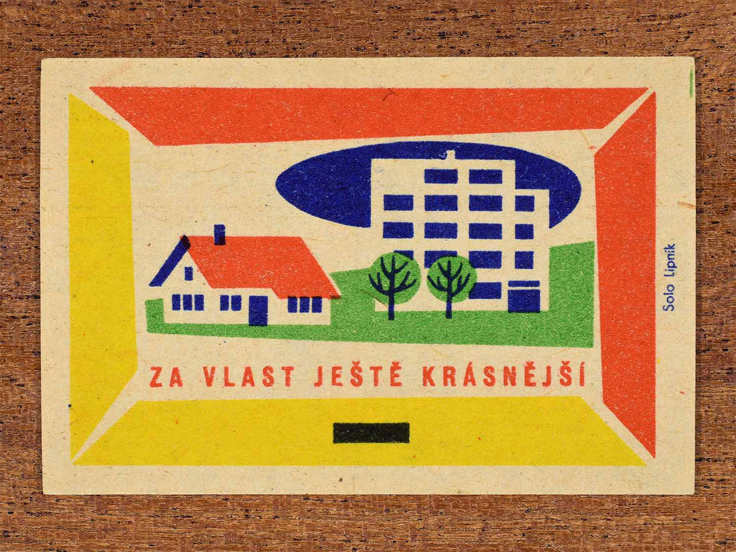 Vintage 1960 Czech matchbox label showing stylised modern apartment buildings and trees framed within bold geometric shapes in red, yellow, green and blue colours. Produced by the Solo Lipník match factory to promote modern housing and urban development.