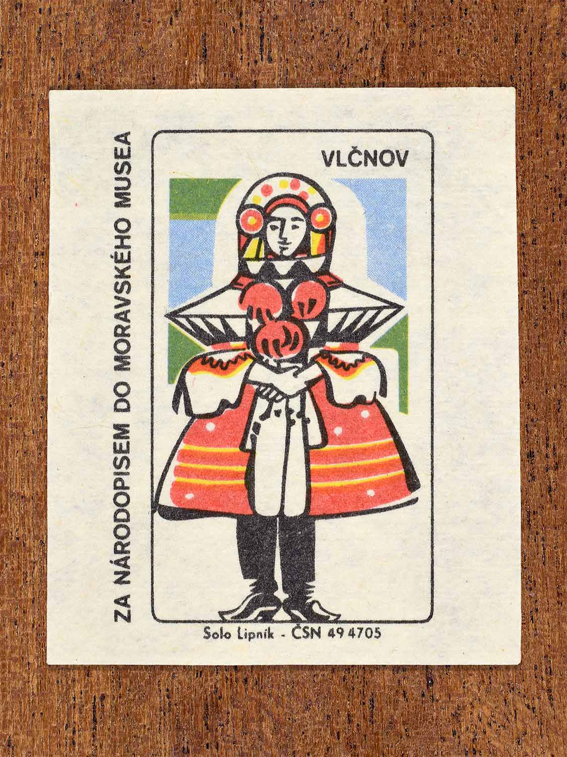 Vintage 1968 Czech matchbox label showing a female folk costume from Vlčnov with a red striped skirt and embroidered bodice. Produced by the Solo Lipník match factory to promote Moravian ethnography through the Moravian Museum.