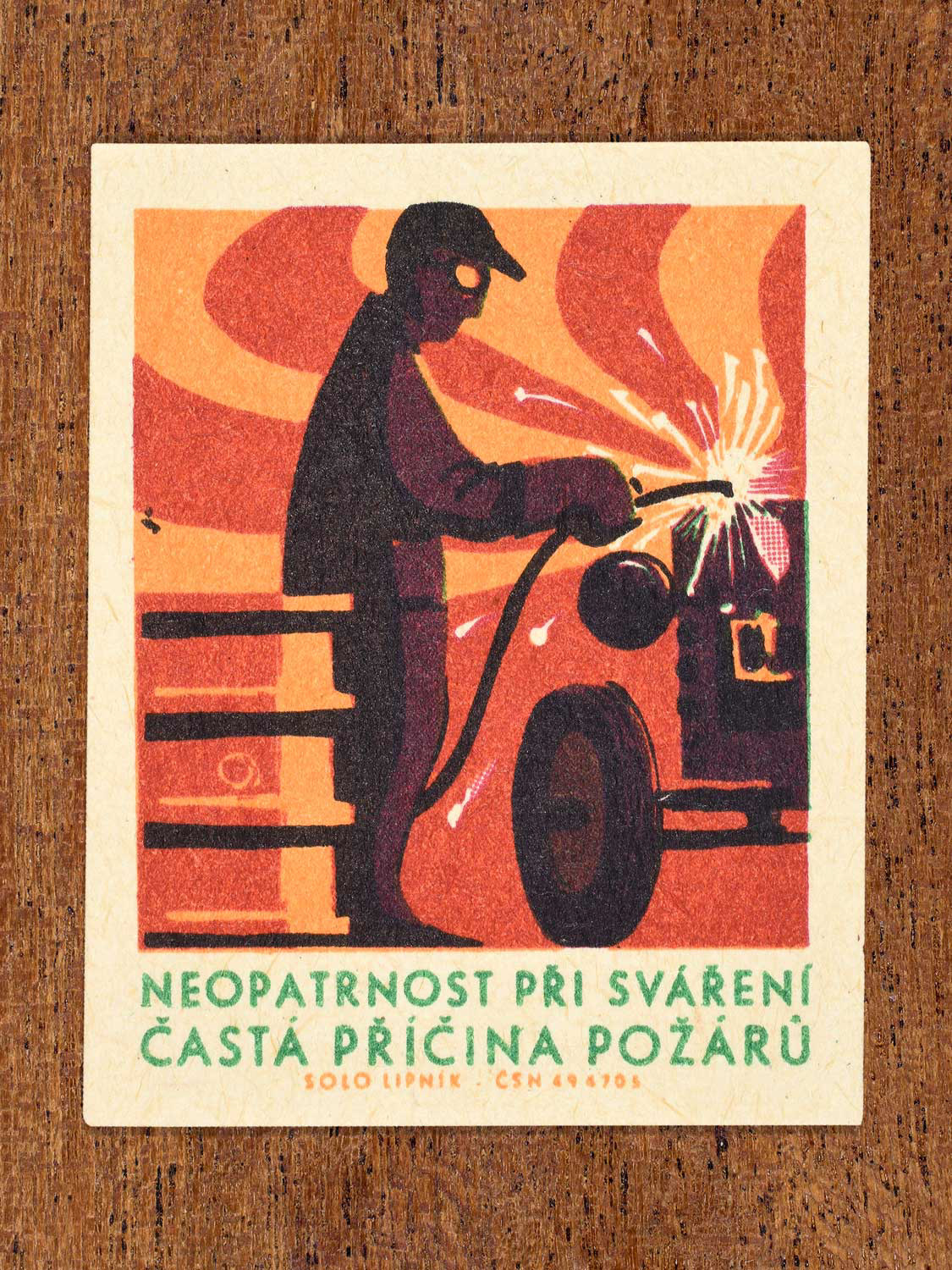 Vintage 1966 Czech matchbox label featuring a man welding a tractor and standing next to a barrel. Produced by Solo Lipník match factory to promote the importance of fire safety precautions.