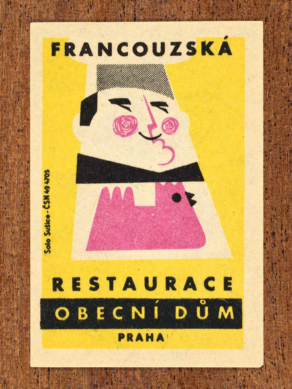 Vintage 1964 Czech matchbox label showing a stylised chef and chicken on a yellow background. Produced by the Solo Sušice match factory to promote a French Restaurant inside Prague's Obecní dům (Municipal House) in Czechoslovakia.