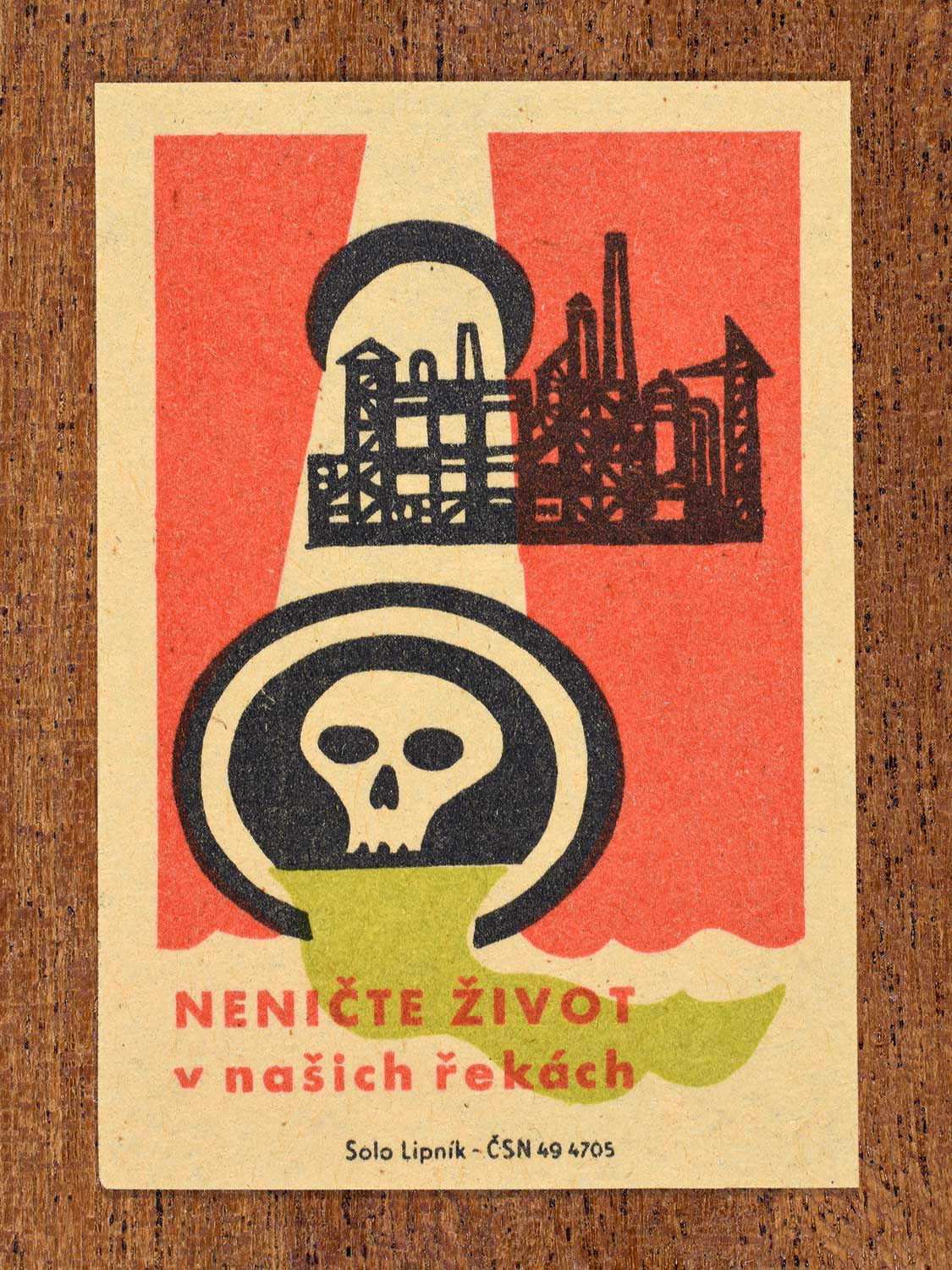 Vintage c. 1963 Czech matchbox label showing a factory pipe releasing toxic waste marked with a skull into a river, in green, red and black colours. Produced by Solo Lipník match factory warning industry not to destroy life in local rivers.