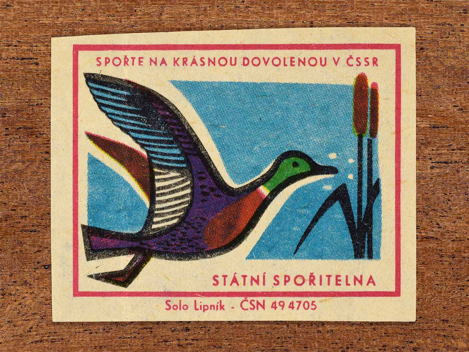 Vintage 1968 Czech matchbox label showing a stylised flying bird beside reeds against a blue sky. Produced by the Solo Lipník match factory to promote saving money for holidays in the Czechoslovak Socialist Republic.
