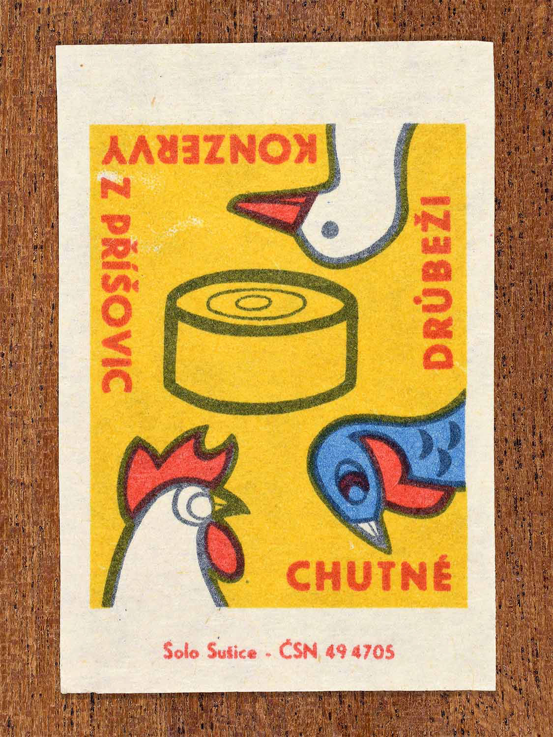 Vintage c. 1966 Czech matchbox label showing a stylised tin of poultry preserves with rooster and hen illustrations in yellow, red and blue. Produced by the Solo Lipník match factory to promote poultry preserves from Příšovice.