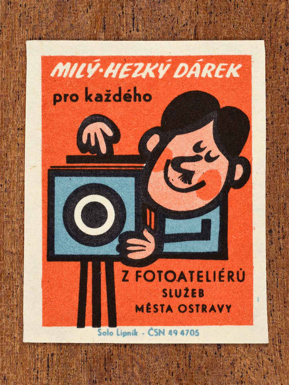 Vintage 1967 Czech matchbox label showing a cartoon man with with photography equipment, on a red background. Produced by the Solo Lipník match factory to advertise municipal photo studio portrait services.