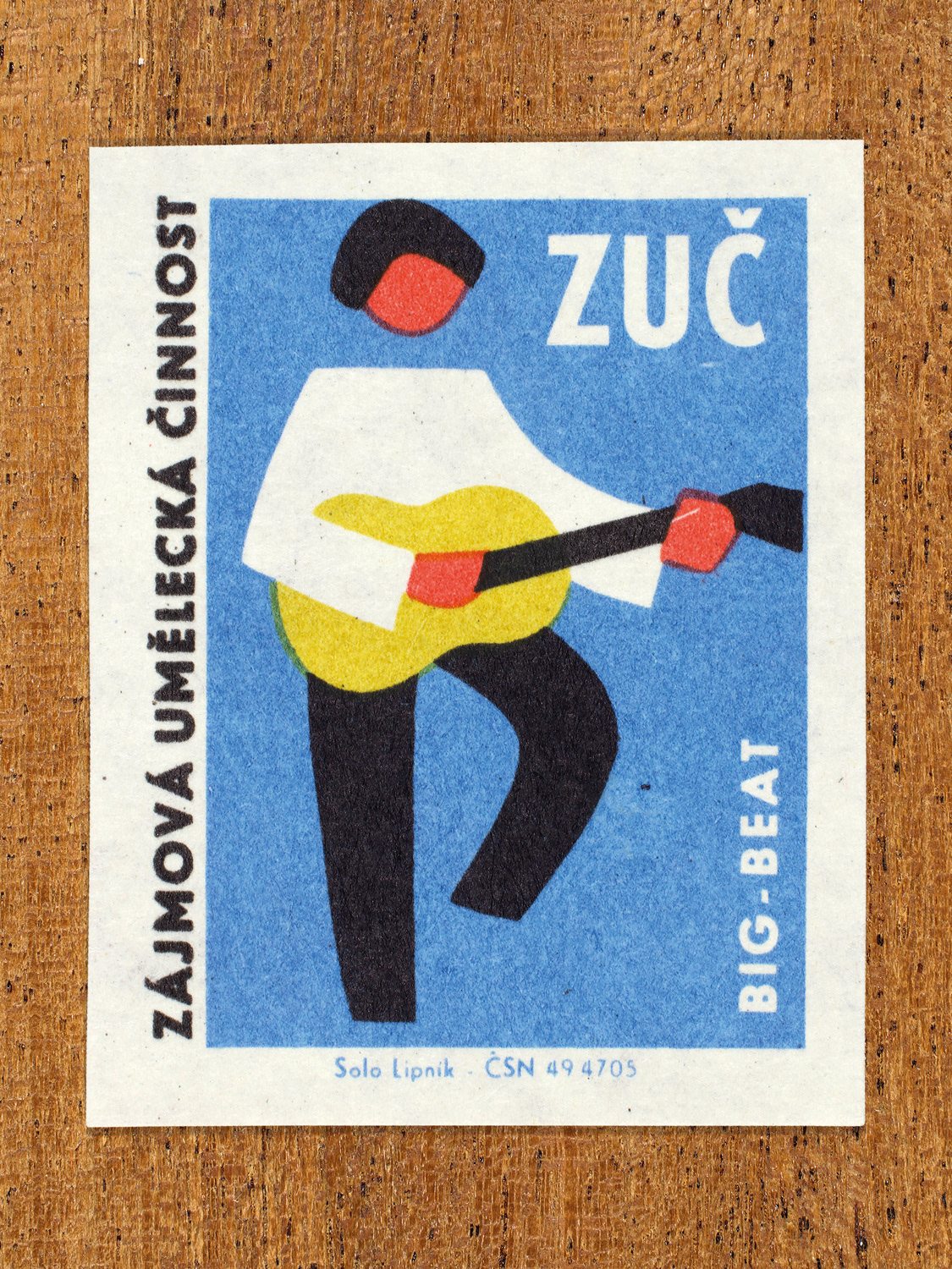 Vintage 1969 Czech matchbox label showing a stylised guitarist stands mid-stride, strumming an electric guitar, in blue, yellow and black colours. Produced by the Solo Lipník match factory to promote state-organised art groups in Czechoslovakia.