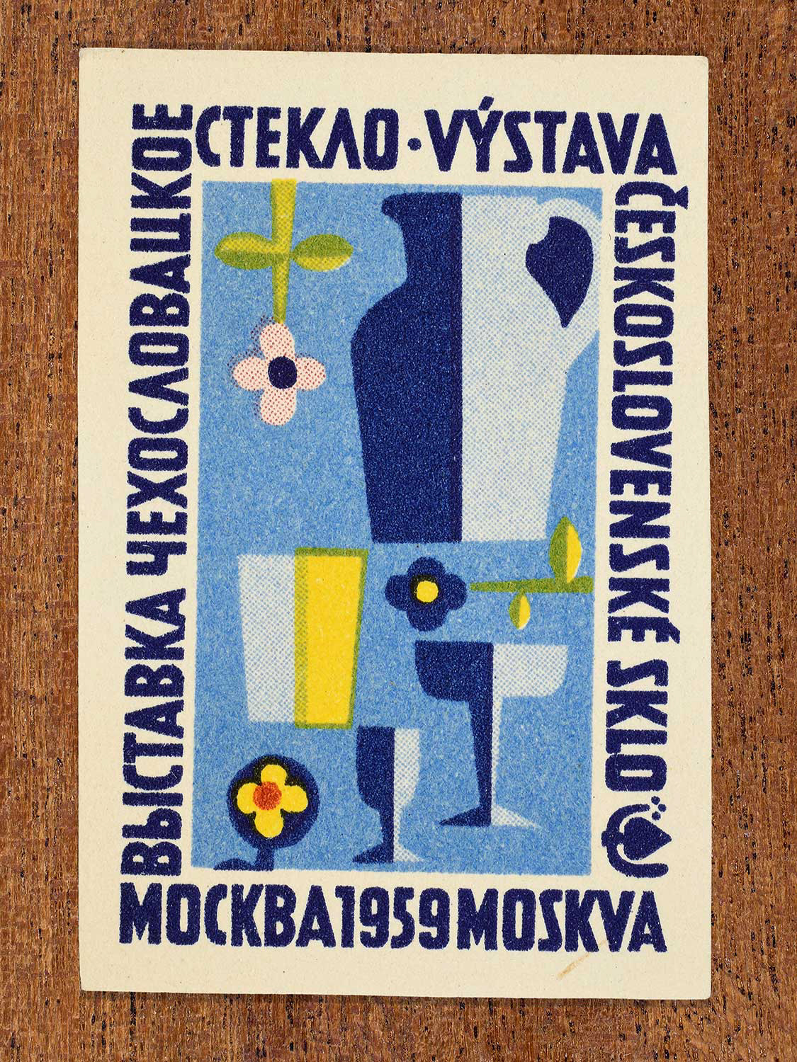 Vintage 1959 Czechoslovak matchbox label showing a collection of stylised glassware in yellow, pink, and blue against a light blue background. Produced as a promotional graphic to demonstrate trends in Czechoslovak glass design as displayed at an exhibition in Moscow.