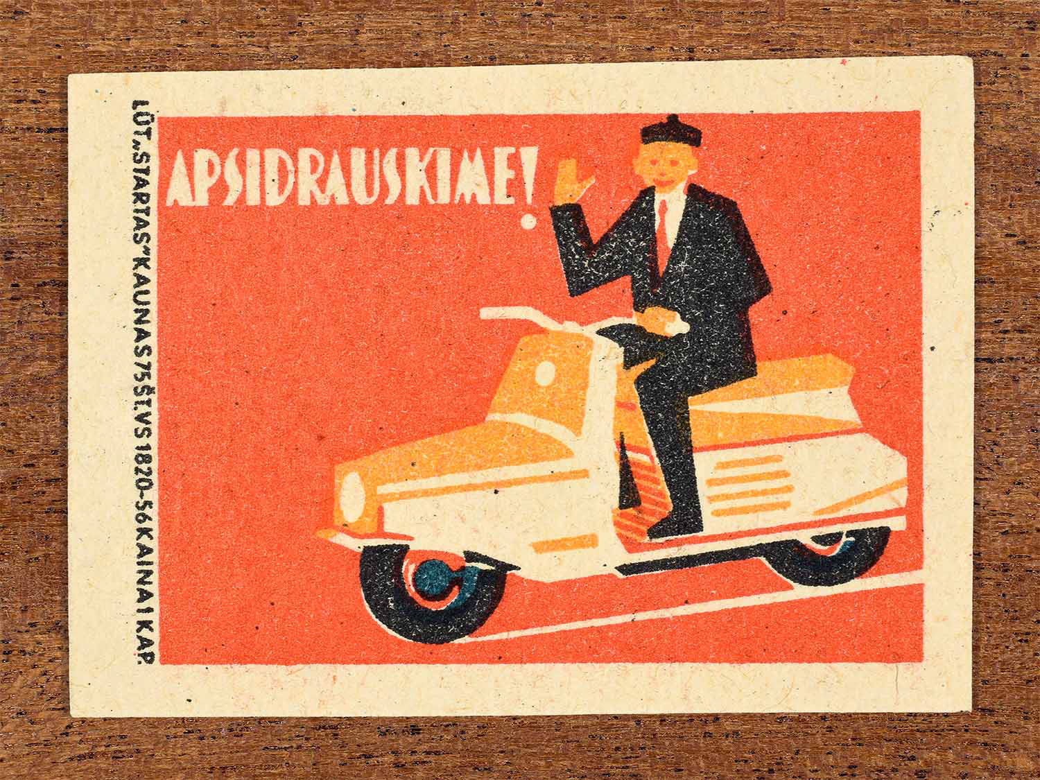 Vintage 1963 Lithuanian matchbox label showing a man on a scooter in red, orange and black colours. Produced by the Startas Kaunas match factory to promote transport insurance.