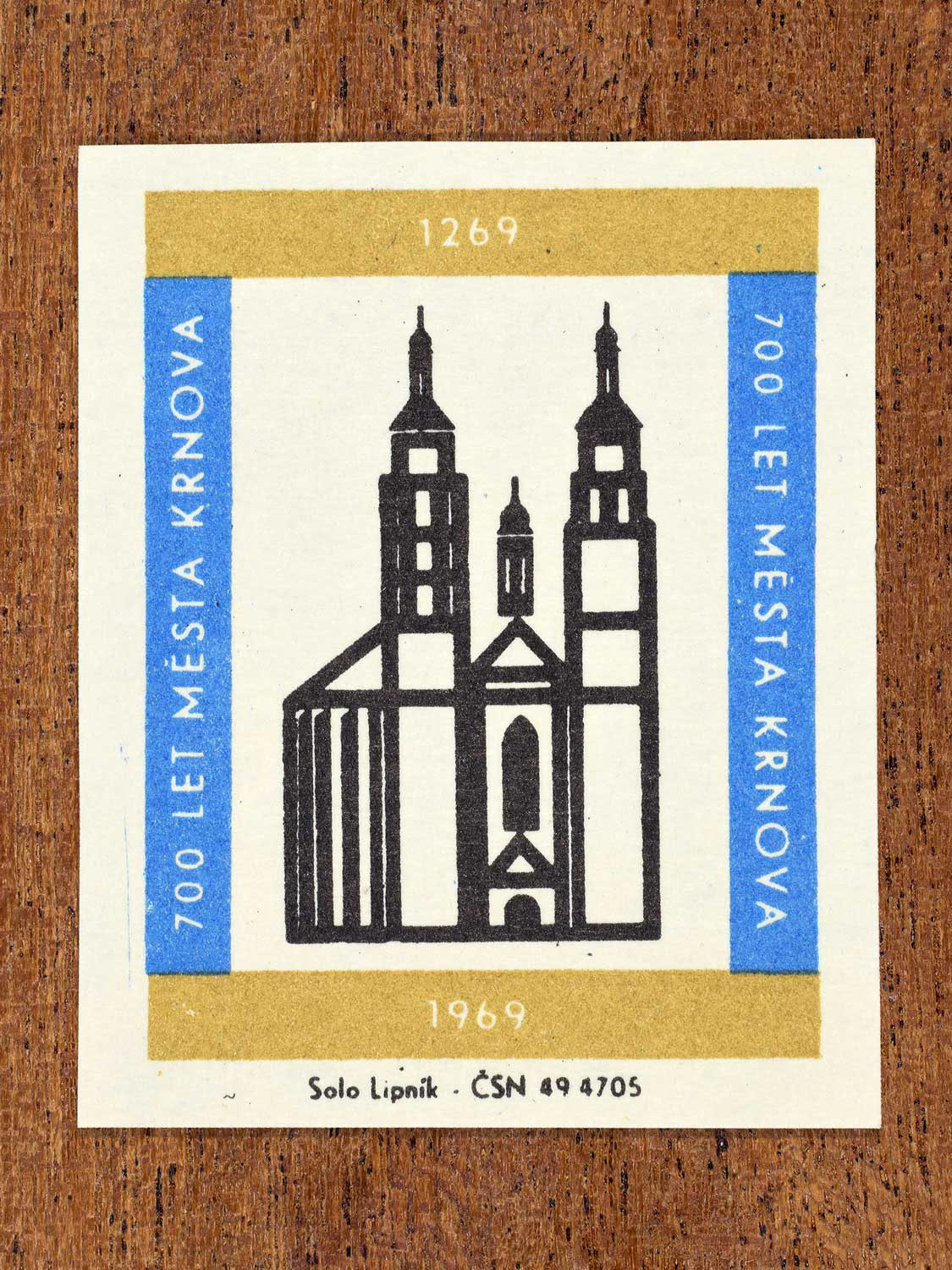 Vintage 1969 Czech matchbox label showing the Parish Church of St. Martin in Krnov, in black with blue and gold framing. Produced by the Solo Lipník match factory to commemorate 700 years of the city of Krnov.