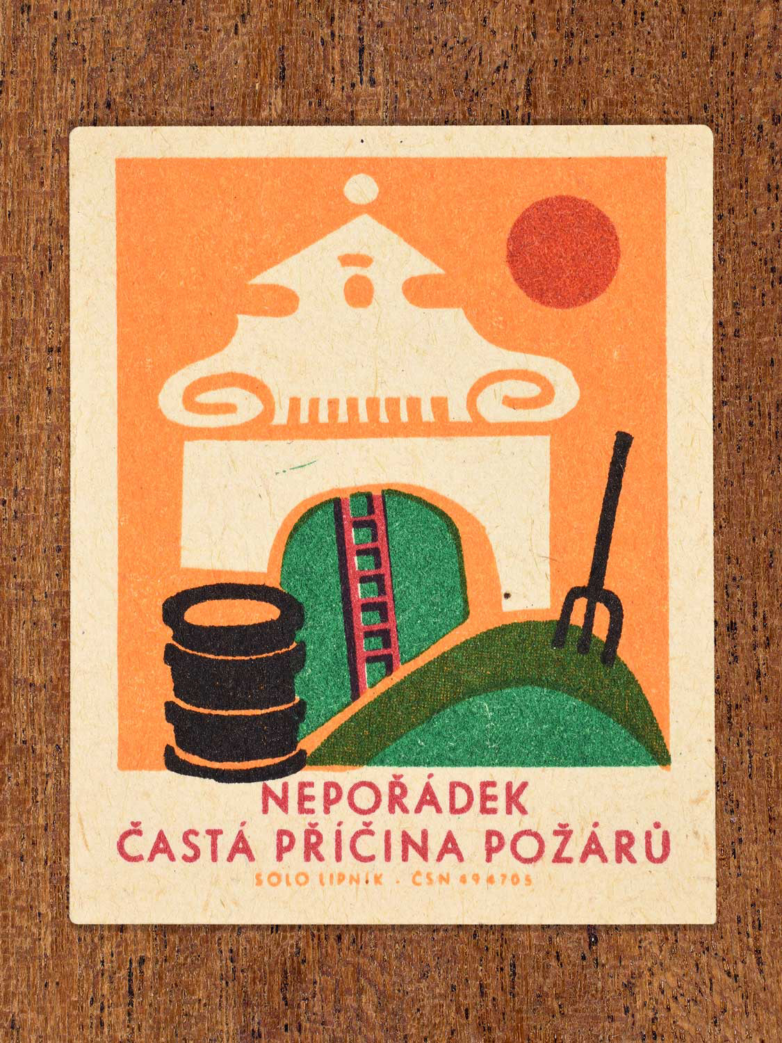 Vintage 1966 Czech matchbox label featuring a building with a barrel, ladder and pile of grass with a pitchfork, on orange background. Produced by Solo Lipník match factory to promote the importance of fire safety precautions.