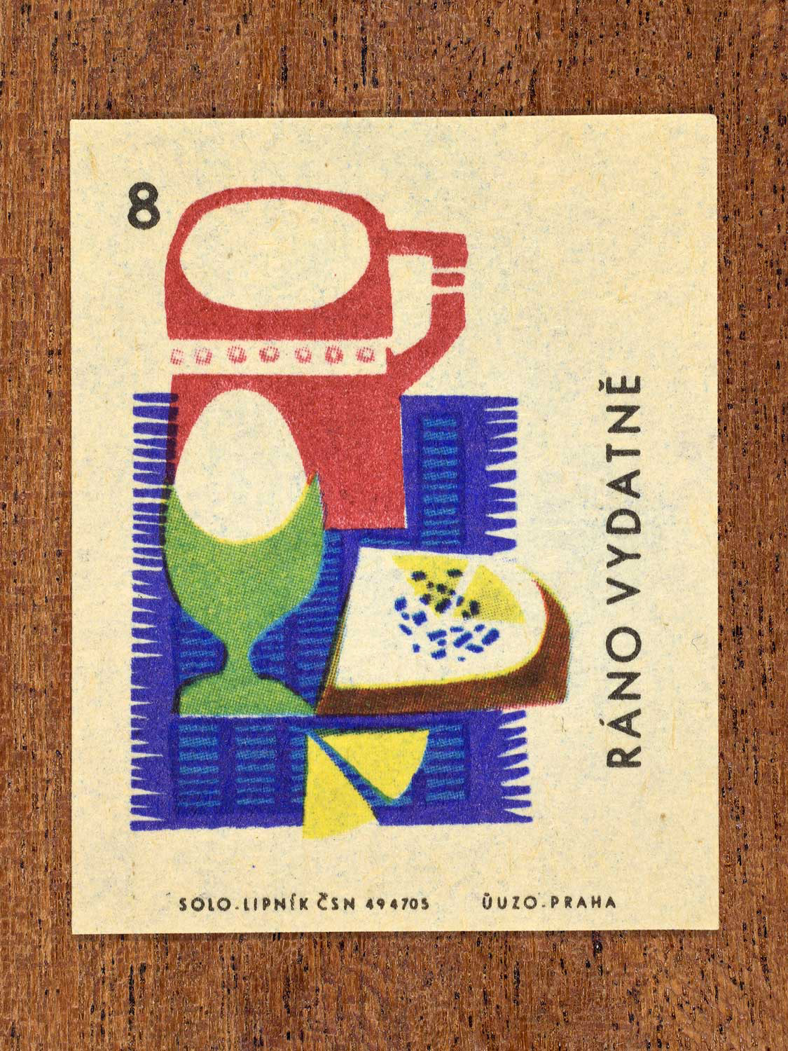 Vintage c. 1965 Czech matchbox label showing showing breakfast foods – egg, bread, cheese, and a mug arranged on a tablecloth. Produced by Solo Lipník match factory to promote the health benefits proper nutrition, daily meal routines, and everyday household habits.