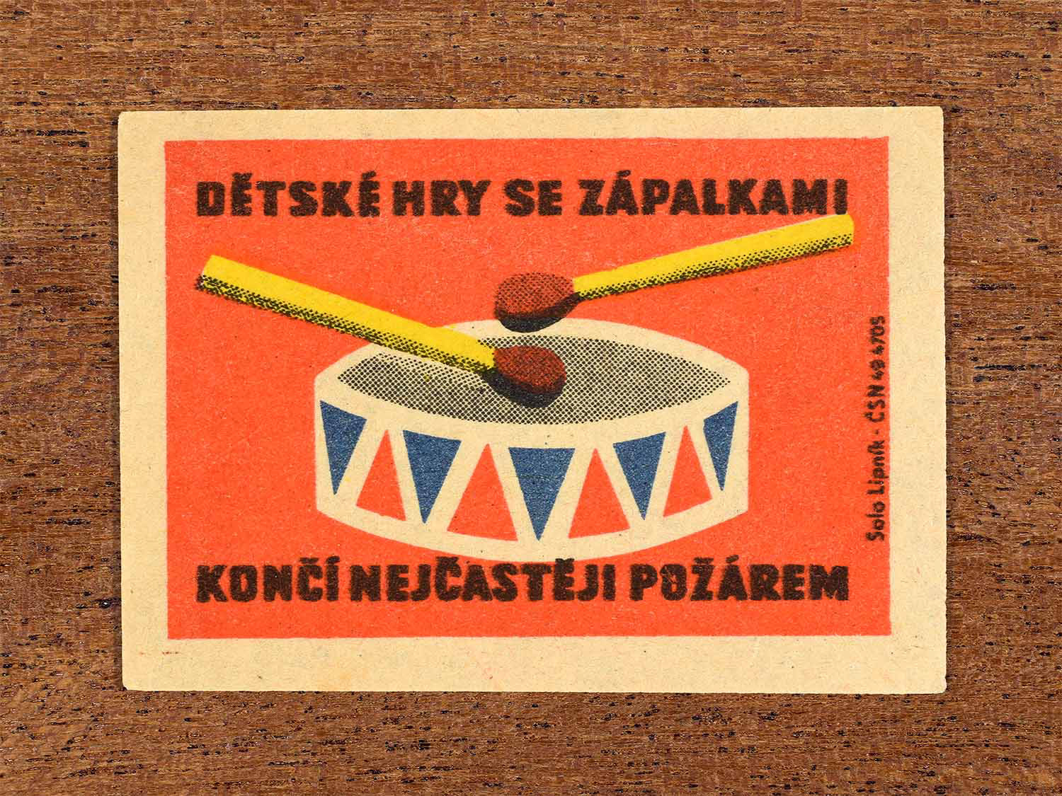 Vintage 1964 Czech matchbox label showing a toy drum and matches as drumsticks in red, yellow and blue colours. Produced by the Solo Lipník match factory to warn that children playing with matches often results in fires.