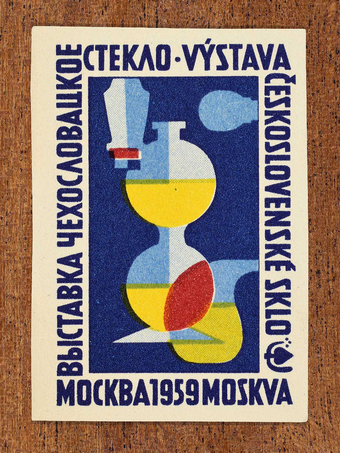 Vintage 1959 Czechoslovak matchbox label showing a stylised yellow, blue, and red abstract glass sculpture against a dark blue background, produced by an unknown factory to promote Czechoslovak artistic glass design at an international cultural event.