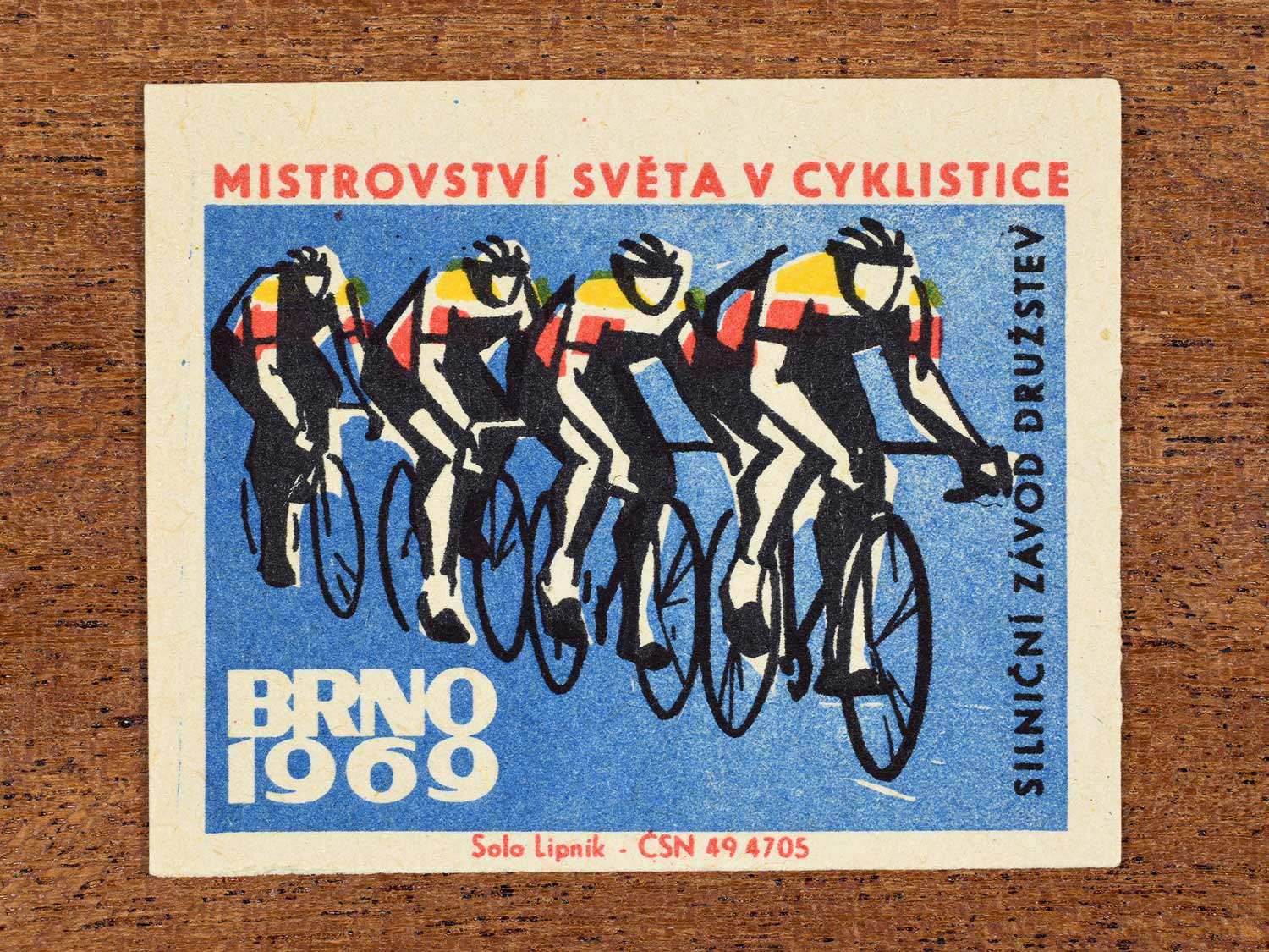 Vintage 1969 Czech matchbox label showing a stylised team of cyclists racing together, on a blue background. Produced by the Solo Lipník match factory to promote team road racing at a cycling championship in Brno, Czechoslovakia.