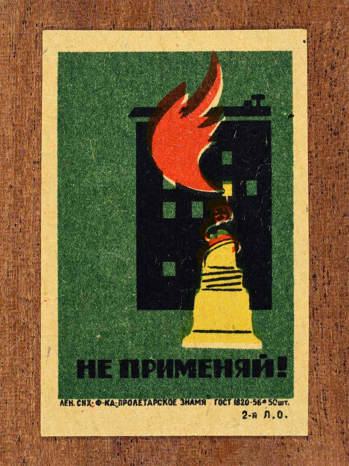 Vintage 1962 Soviet matchbox label showing a building fire hazard warning. In green, red, yellow and black colours. Produced by the Proletarian Banner match factory to discourage unsafe use of fire-related tools.