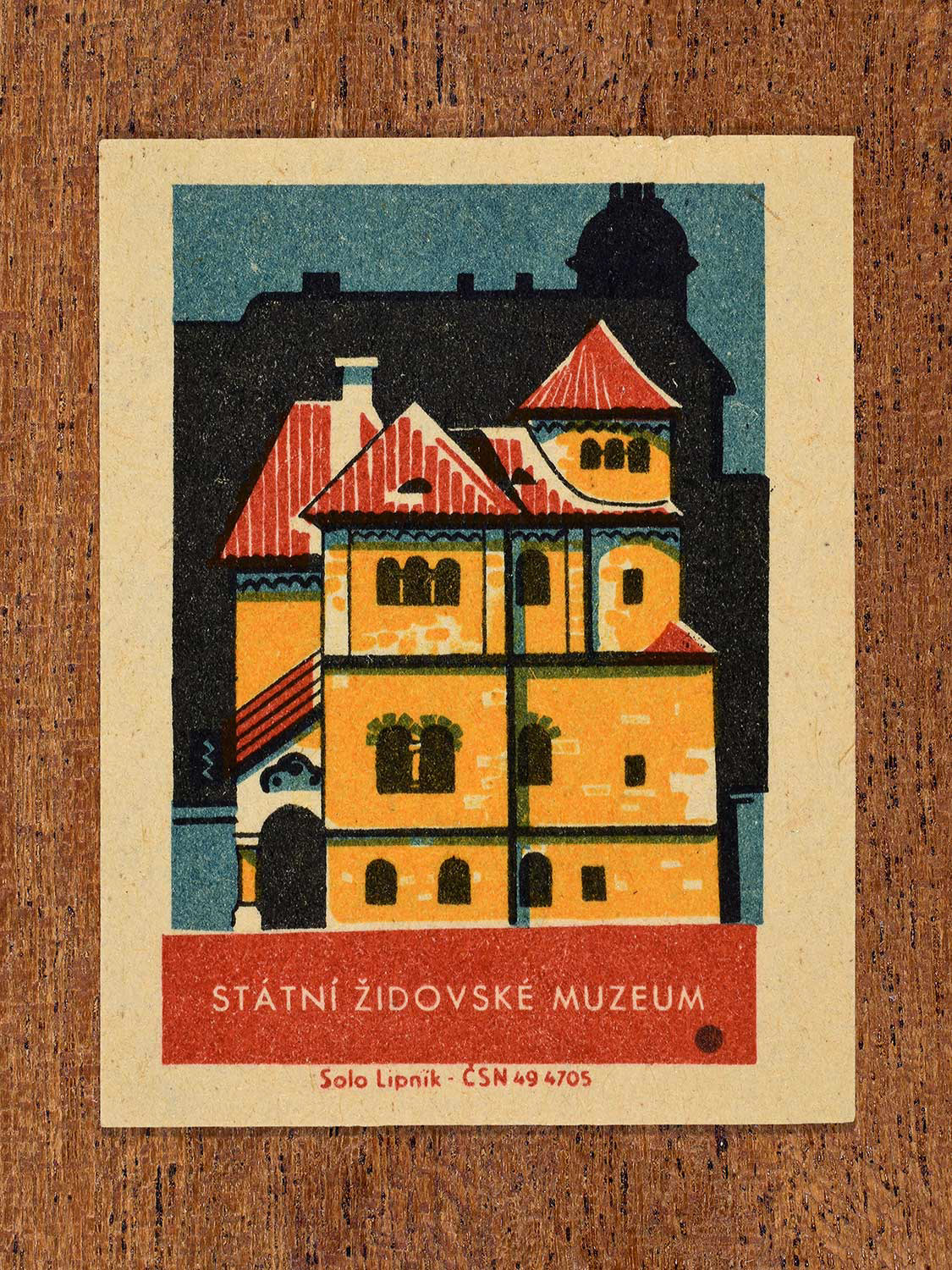 Vintage 1964 Czechoslovakia matchbox label showing the Státní Židovské Muzeum (State Jewish Museum) in yellow, red and teal colours. Produced by the Solo Lipník match factory to promote domestic historical heritage and municipal institutions across the state.