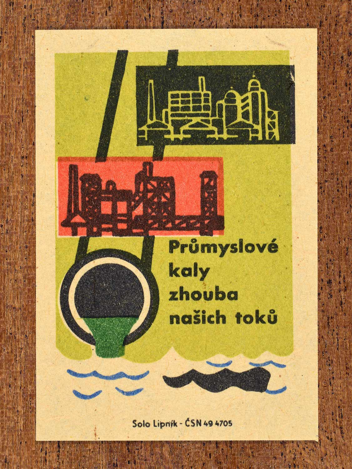 Vintage c. 1963 Czech matchbox label featuring a factory pipe releasing green sludge into a river with green, red and black colours. Produced by Solo Lipník match factory warning that industrial sludge ruins waterways.