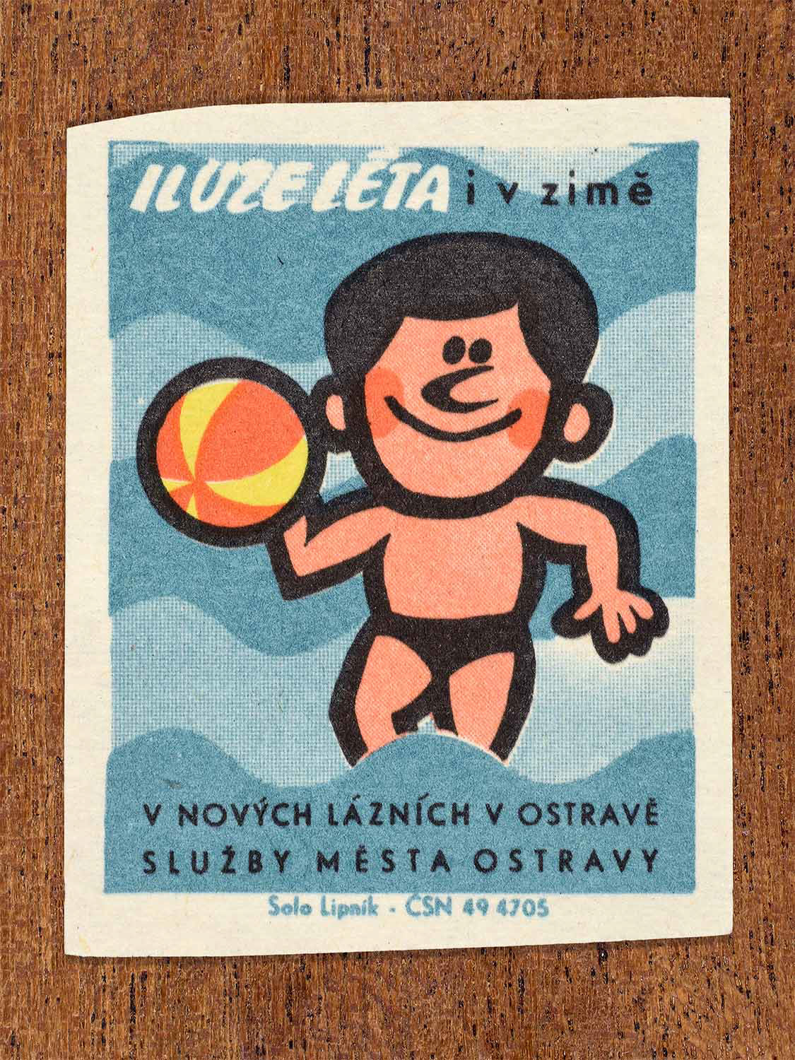 Vintage 1967 Czech matchbox label showing a cartoon man holding a beach ball, on a blue wavy background. Produced by the Solo Lipník match factory to promote the new public baths in Ostrava.