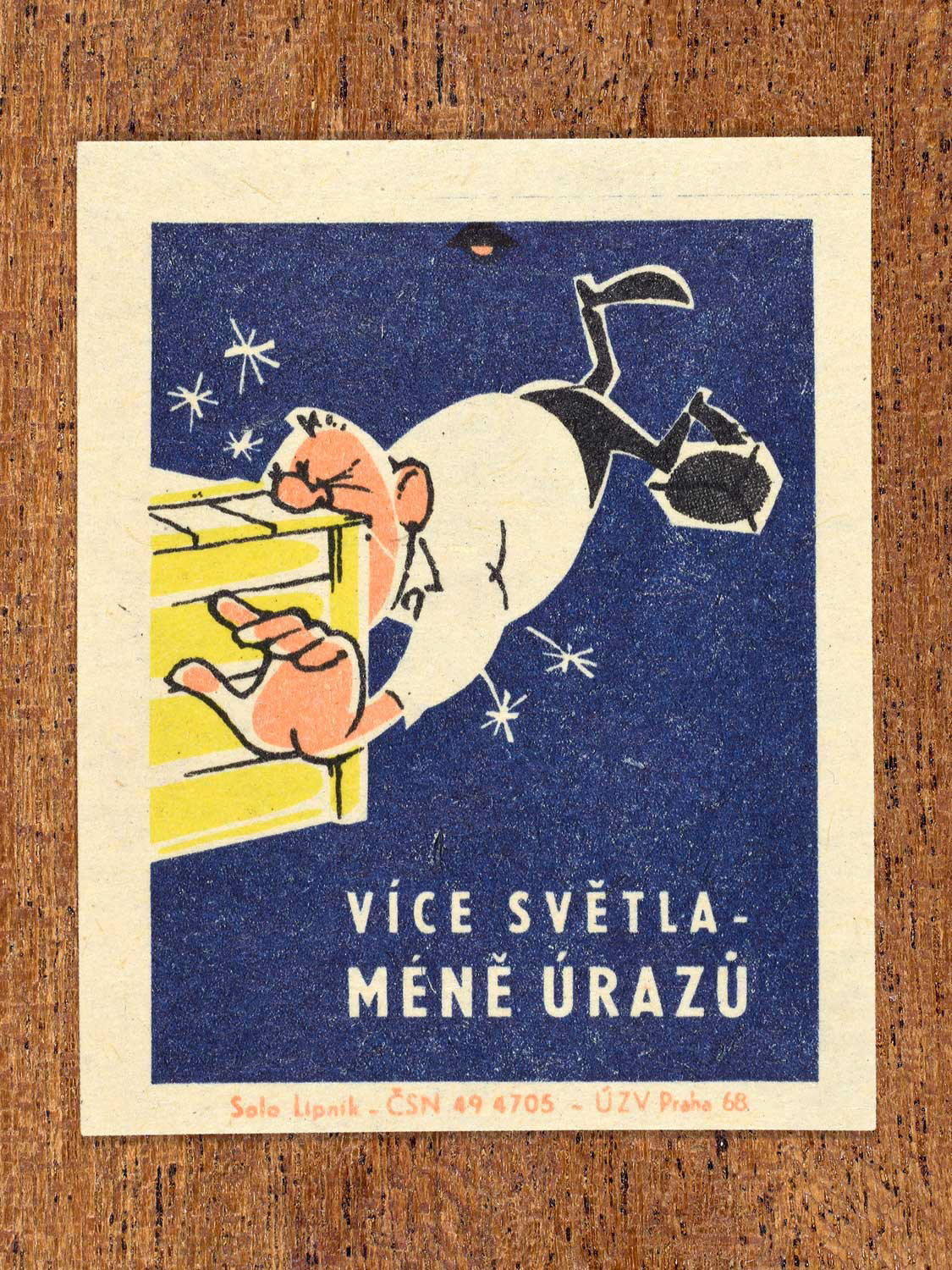 Vintage 1968 Czech matchbox label featuring a cartoon person tripping and falling nose-first into a big yellow box, on blue background. Produced by Solo Lipník match factory to promote proper lighting and maintenance for eye health and safe work practices.