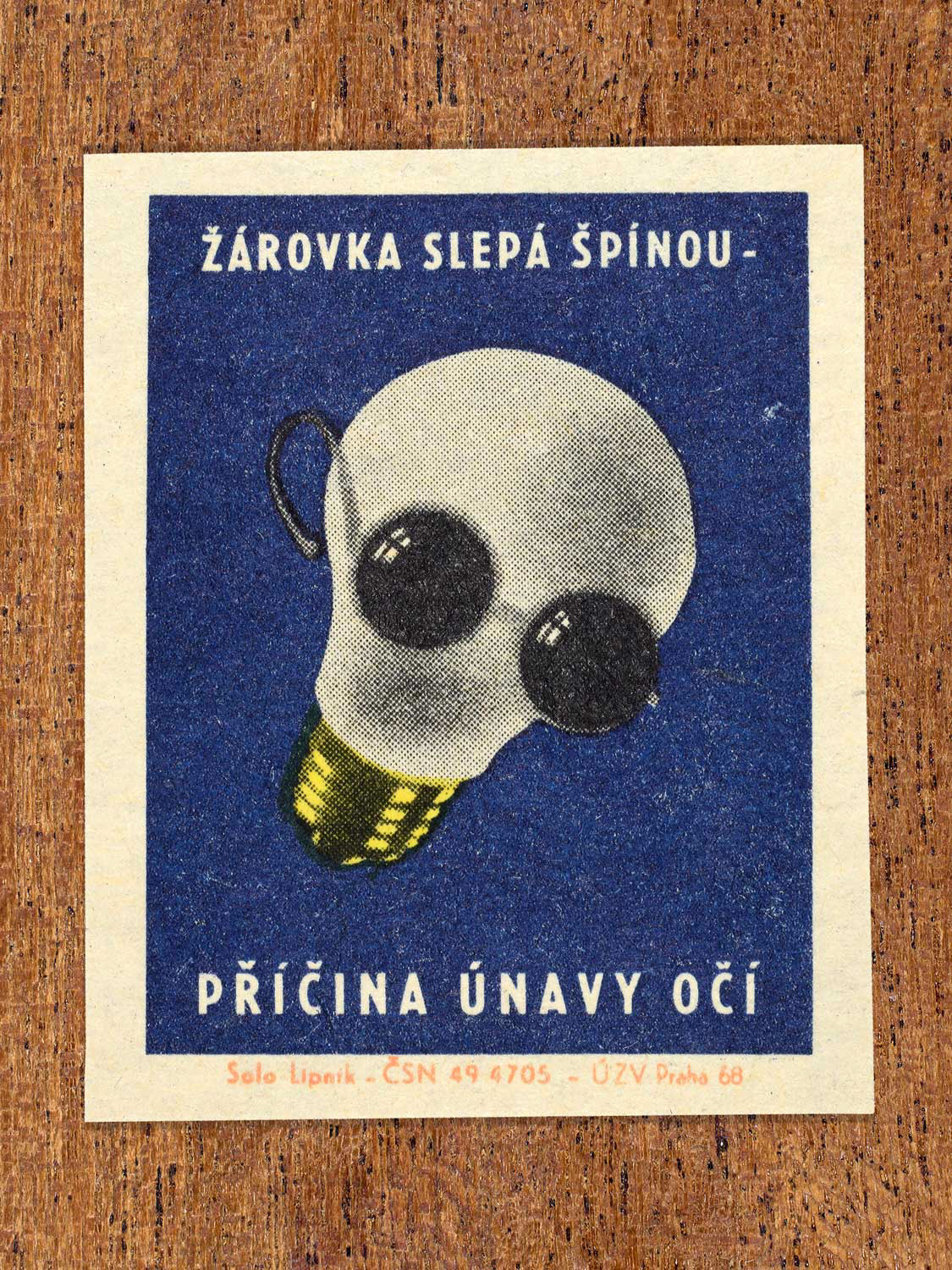 Vintage 1968 Czech matchbox label featuring a light bulb wearing sunglasses, on blue background. Produced by Solo Lipník match factory to promote proper lighting and maintenance for eye health and safe work practices.