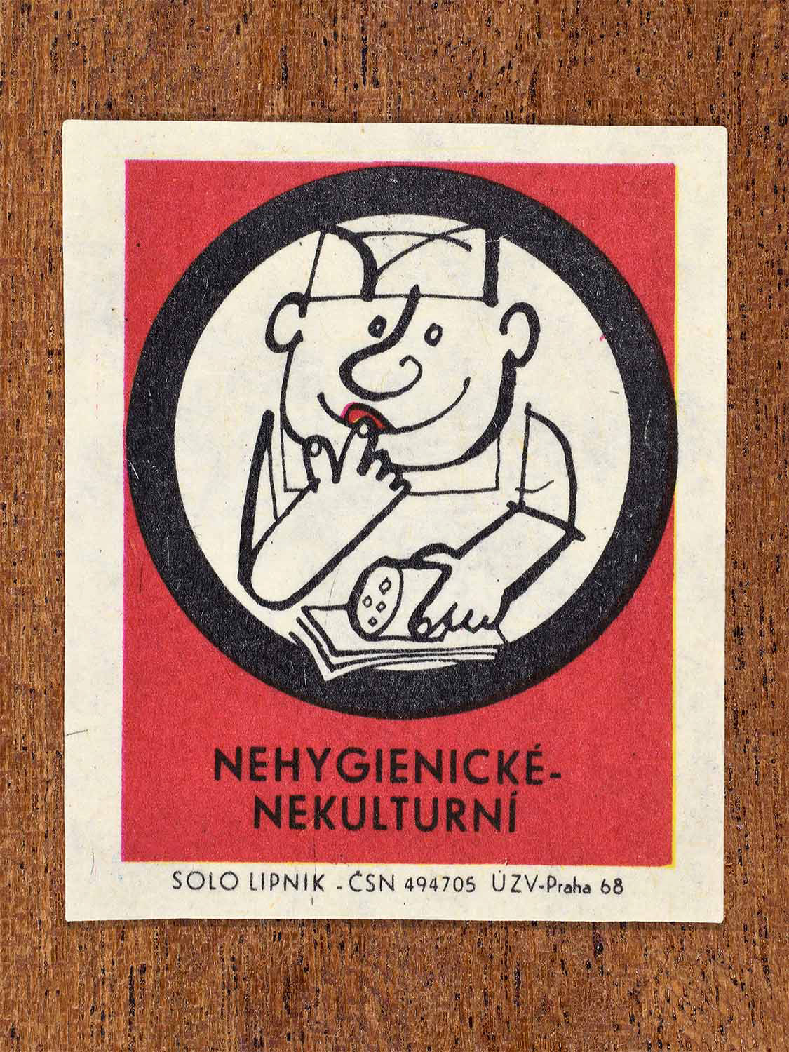 Vintage c. 1968 Czech matchbox label showing a worker touching food and their mouth, framed in a circle and on a red background. Produced by the Solo Lipník match factory to discourage unhygienic food handling practices.