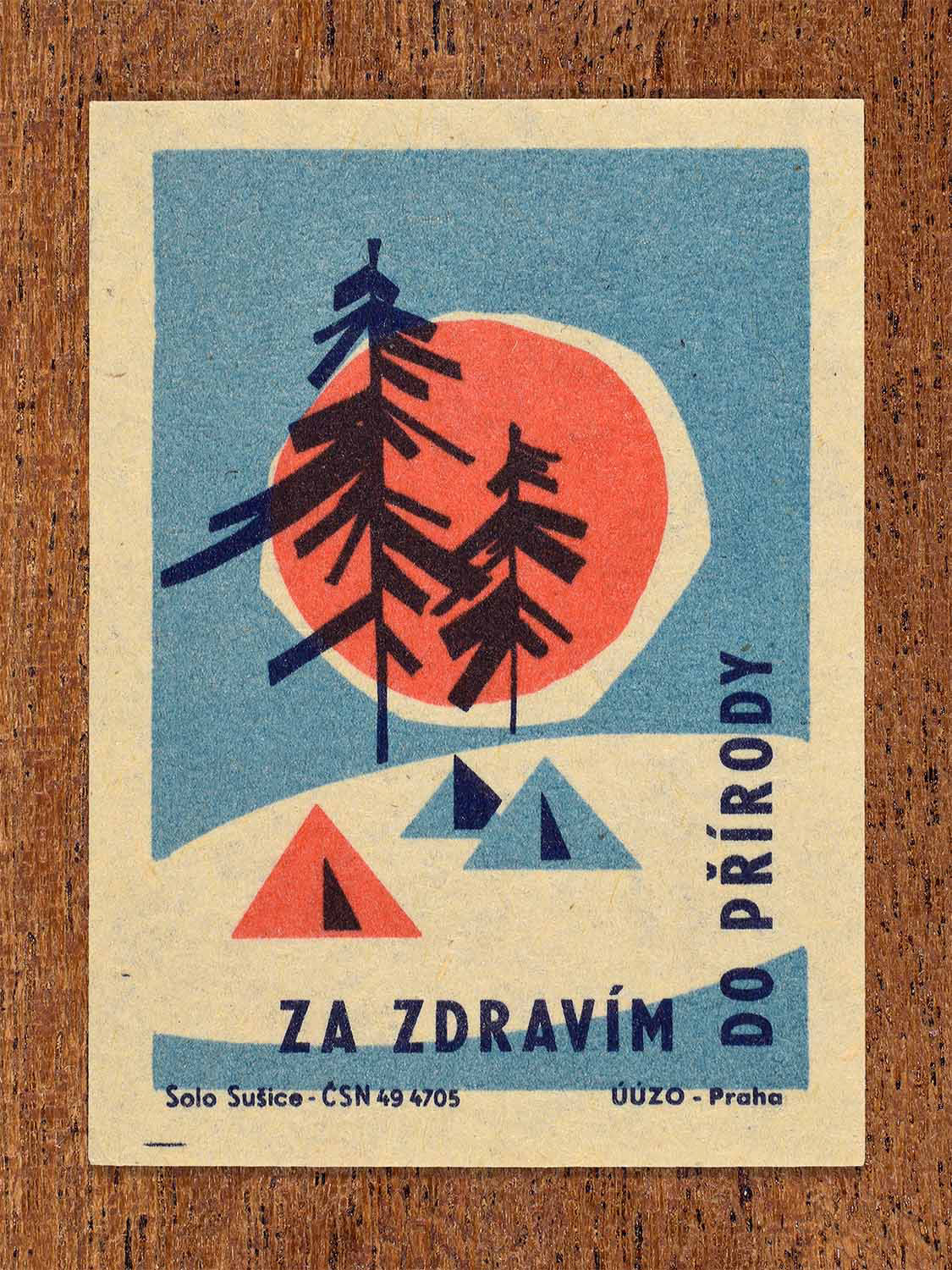 Vintage c. 1964 Czech matchbox label showing a stylised forest landscape with tents and sun in blue and red colours. Produced by the Solo Sušice match factory to promote spending time in nature for better health.