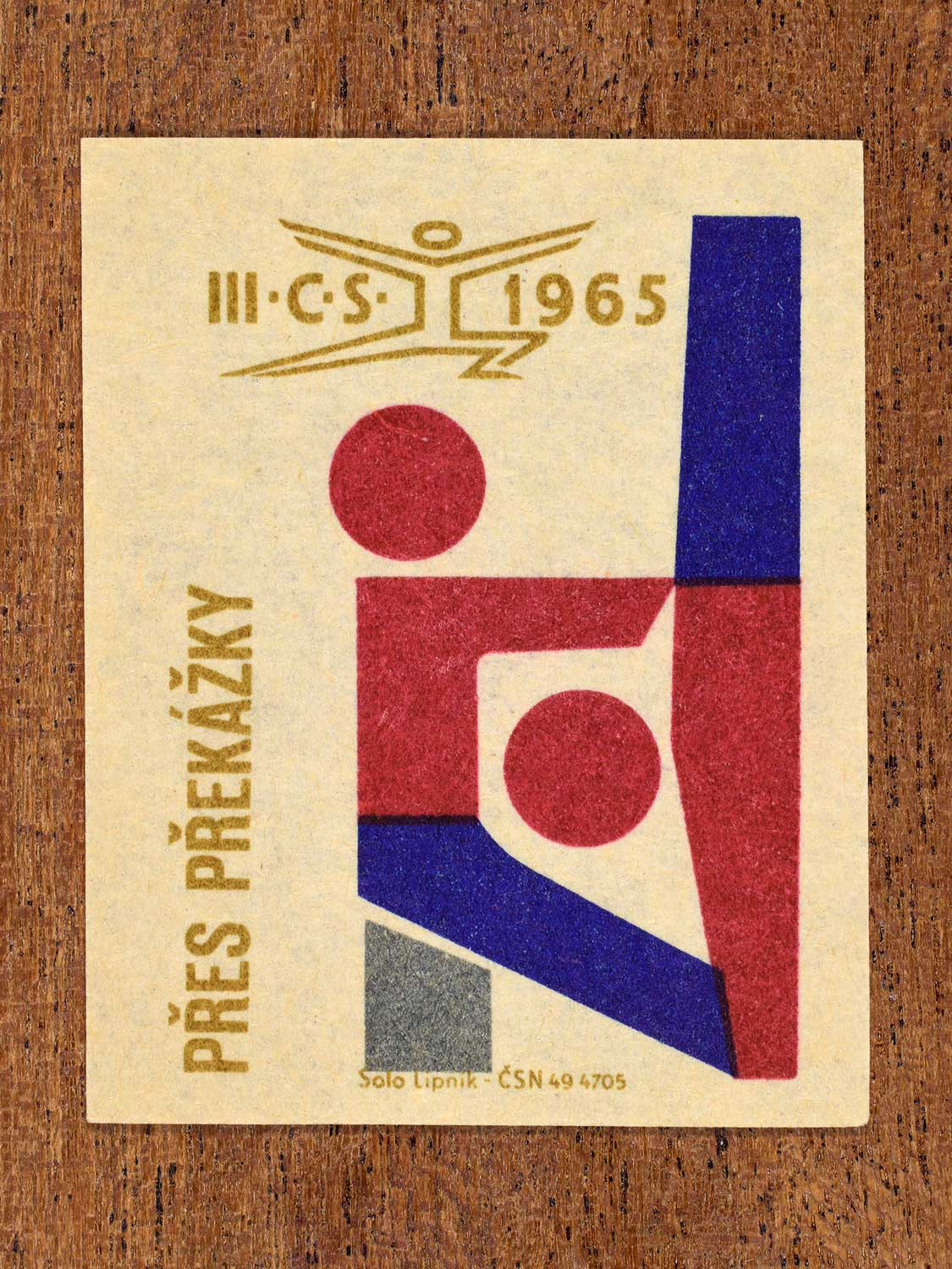 Vintage 1965 Czechoslovak matchbox label showing two abstract gymnastics figures, in blue, red and gold colours. Produced by the Solo Lipník match factory to promote physical fitness and sporting achievement.