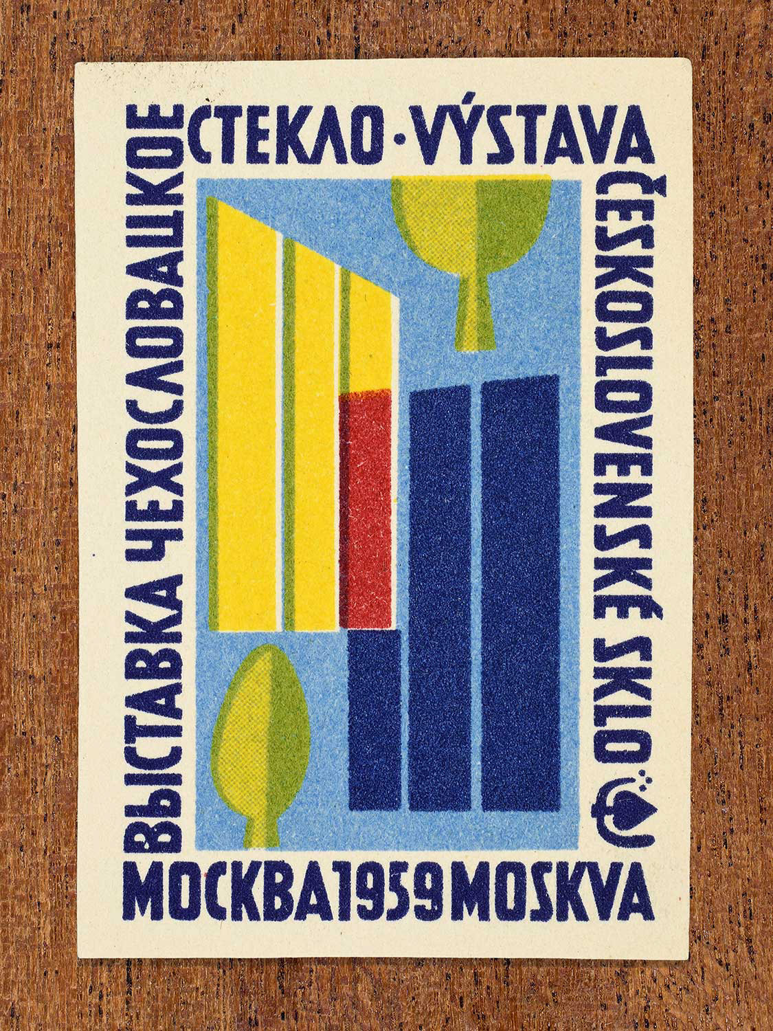 Vintage 1959 Czechoslovak matchbox label showing an abstract glass sculpture in yellow, blue, and red on a dark blue background. Produced by an unknown factory to promote Czechoslovak artistic glass design at an international cultural event in Moscow.