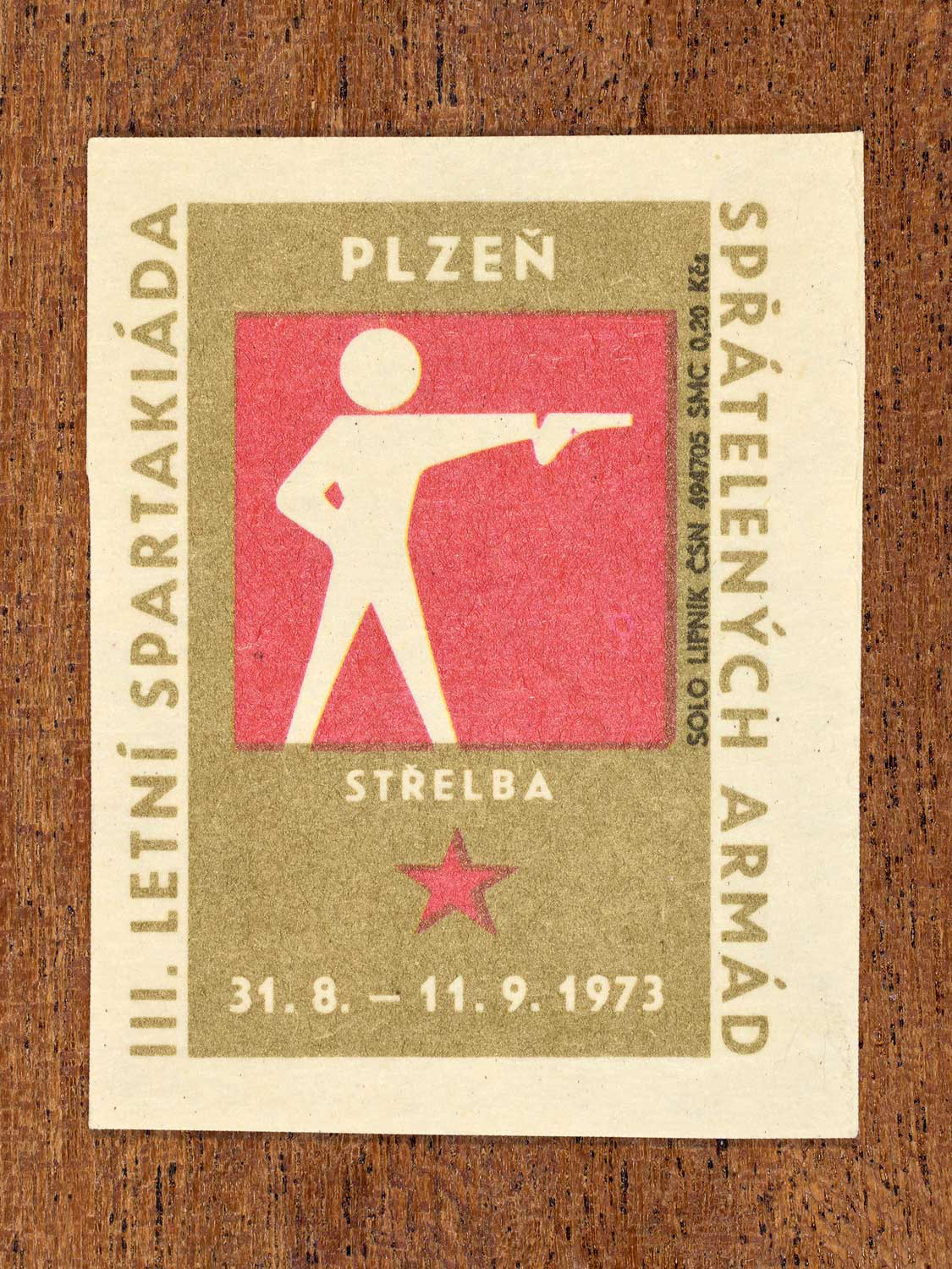 Vintage 1973 Czech matchbox label showing a simplified white figure aiming a handgun on a red and gold background. Produced by the Solo Lipník match factory to promote physical training and demonstrate collective military readiness among allied armies.