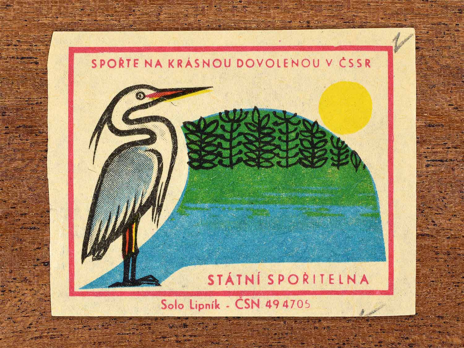 Vintage 1968 Czech matchbox label showing a heron standing beside a lake with forest and sun in the background. Produced by the Solo Lipník match factory to promote saving money for holidays in the Czechoslovak Socialist Republic.