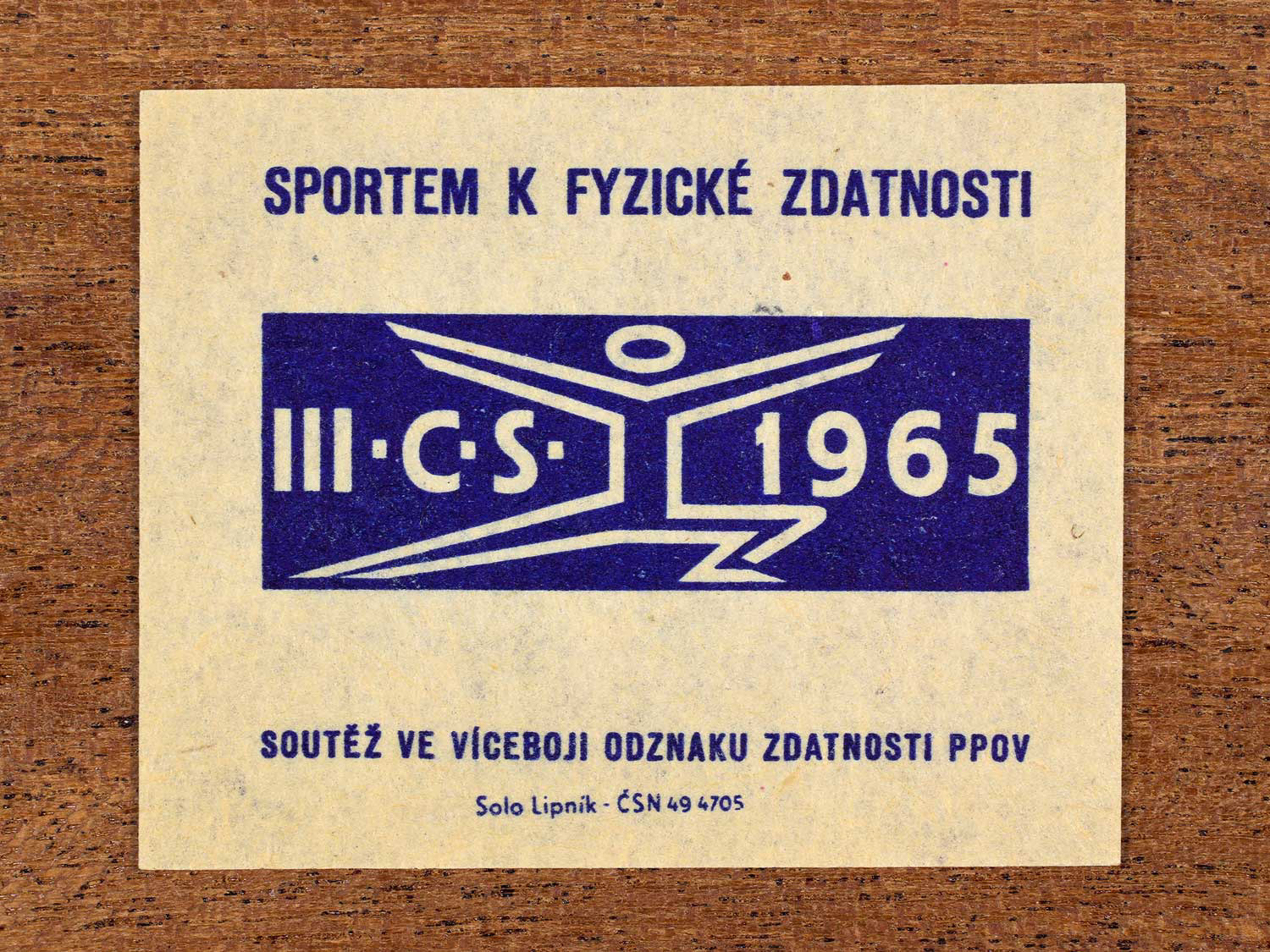 Vintage 1965 Czechoslovak matchbox label showing a symbolic athletic figure in blue. Produced by the Solo Lipník match factory to promote physical fitness and sporting achievement.