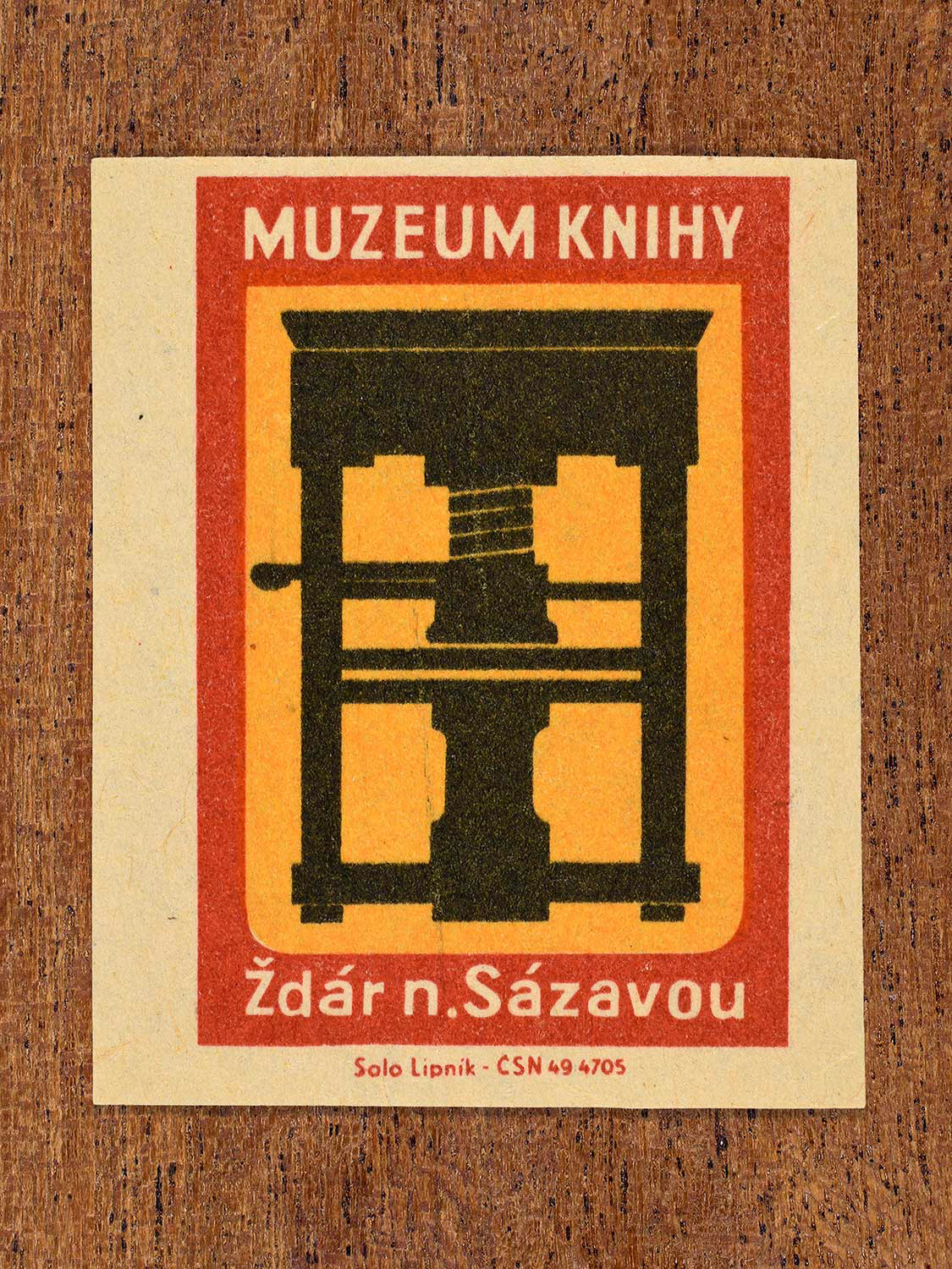 Vintage 1964 Czechoslovakia matchbox label showing a silhouette of a mechanical Gutenburg-style printing press in black, yellow and red colours. Produced by the Solo Lipník match factory to promote the Muzeum Knihy (Museum of the Book) in Žďár n. Sázavou, a town in Czechoslovakia.