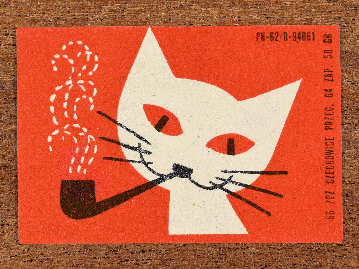 Vintage 1966 Polish matchbox label showing a stylised white cat smoking a pipe with white dotted smoke on a red background. Produced by the Czechowice match factory in Poland as retail packaging for safety matches.