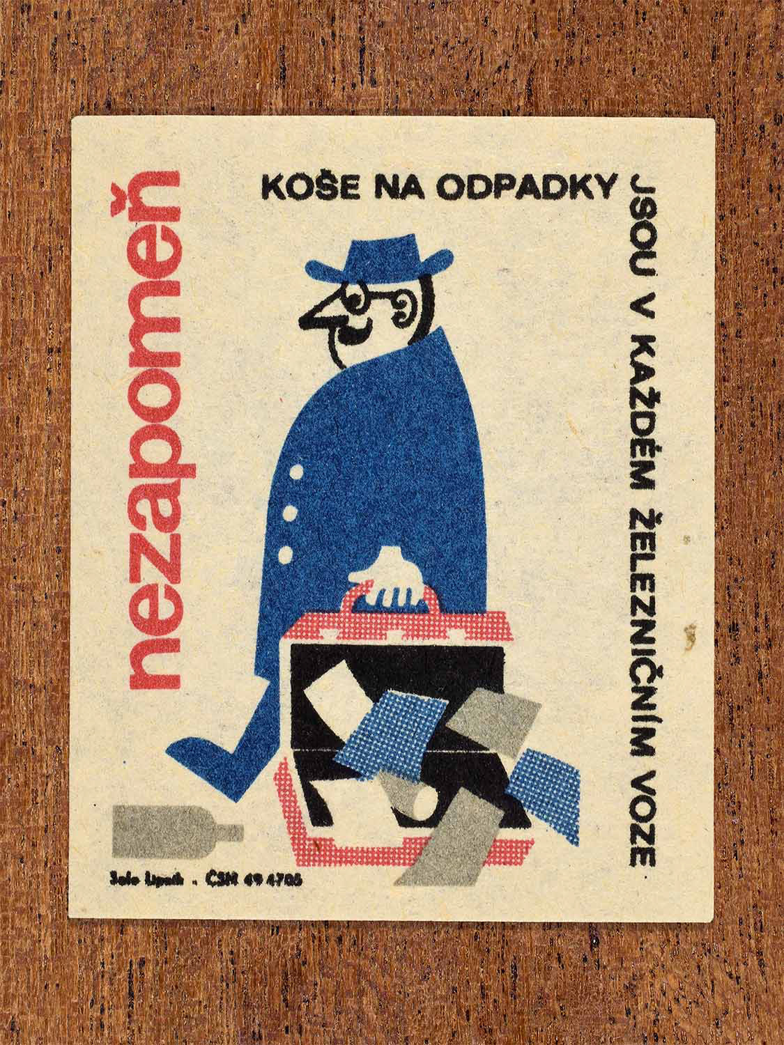 Vintage c. 1964 Czech matchbox label showing a man dropping papers from an open briefcase onto a carriage floor, illustrated in blue, red and black. Produced by the Solo Lipník match factory to discourage littering on railway carriages.