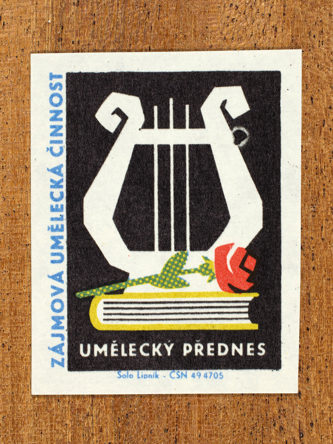 Vintage 1969 Czech matchbox label showing a stylised lyre standing behind a book and single red rose, on a black background. Produced by the Solo Lipník match factory to promote state-organised art groups in Czechoslovakia.