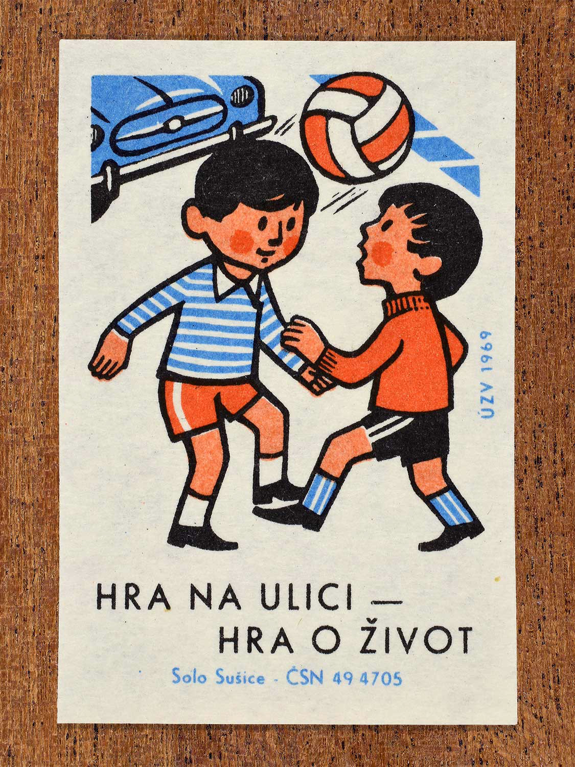 Vintage 1969 Czech matchbox label showing two young boys playing football/ soccer in the middle of a street with a blue car approaching in the background. Produced by the Solo Sušice match factory to promote childhood safety and prevent street playing hazards.