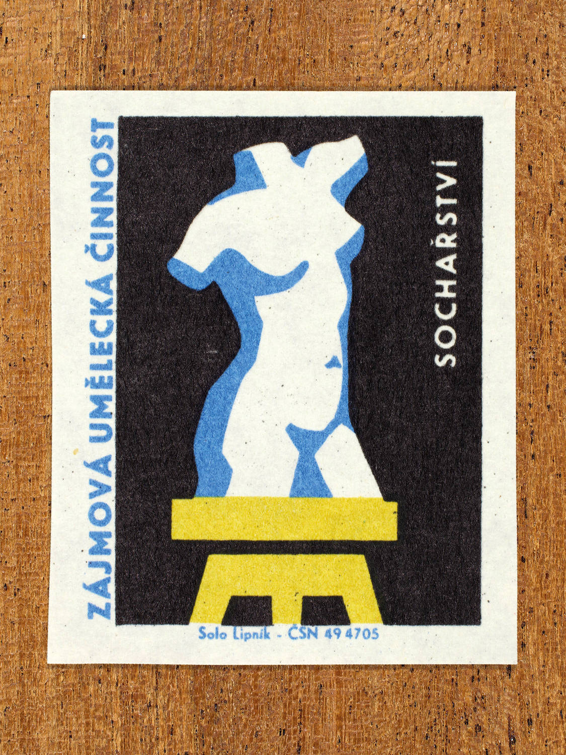 Vintage 1969 Czech matchbox label showing a stylised stone statue of a torso standing on a plinth, in blue, yellow and black colours. Produced by the Solo Lipník match factory to promote state-organised art groups in Czechoslovakia.