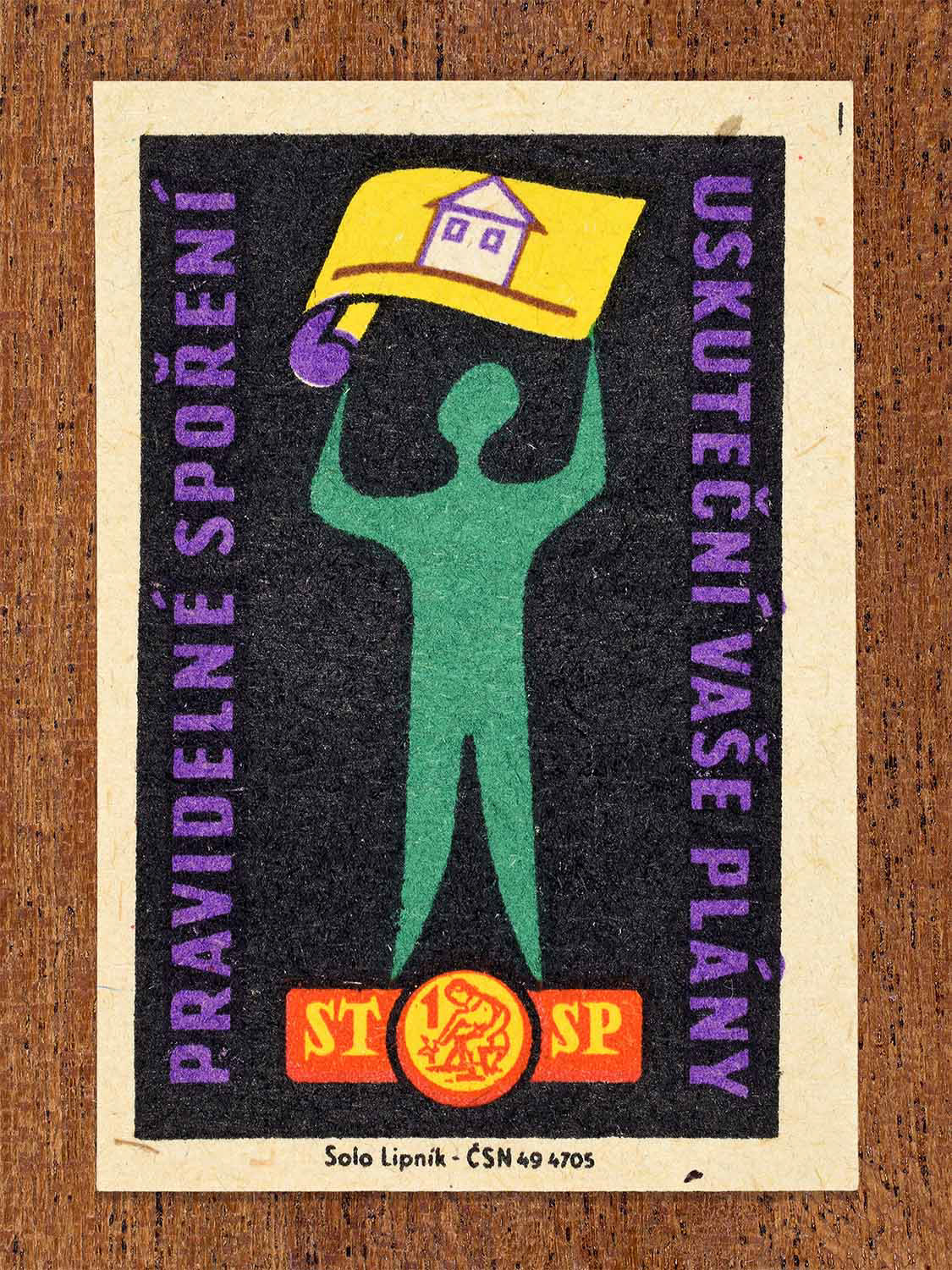 Vintage 1960 Czech matchbox label showing a figure lifting a drawing of house above their head, in black, green and purple colours. Produced by the Solo Lipník match factory to promote regular saving as a way to achieve personal plans.