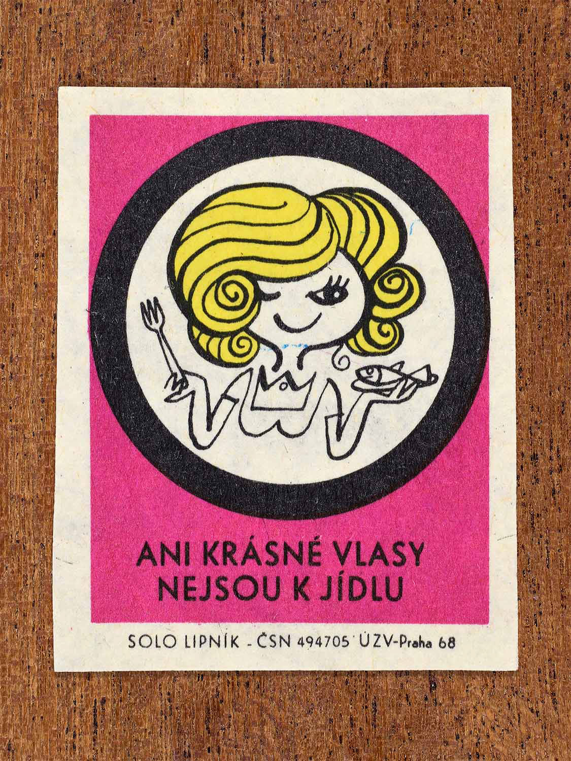 Vintage c. 1968 Czech matchbox label showing a woman with uncovered hair while handling food, framed in a circle and on a pink background. Produced by the Solo Lipník match factory to warn against hair contaminating food.