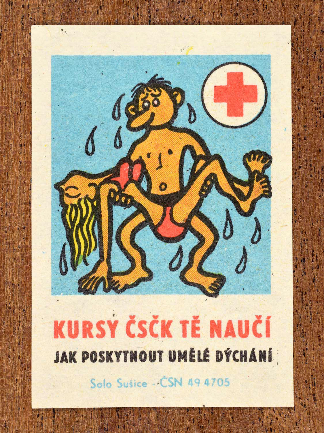 Vintage c. 1966 Czech matchbox label showing a man carrying an unconscious woman. Produced by the Solo Sušice match factory to promote first-aid education and lifesaving resuscitation techniques in cooperation with the Czechoslovak Red Cross.