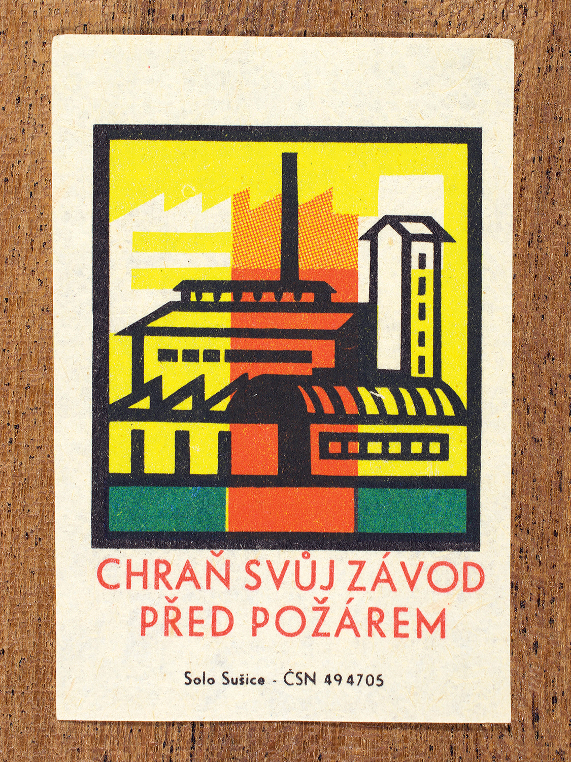1968 Czechoslovak matchbox label by Solo Sušice showing a brightly colored factory with smokestacks. Used as a public service message reminding factories and workplaces to follow fire safety precautions. Label 3 of 10 in the Fire Hazards Series.