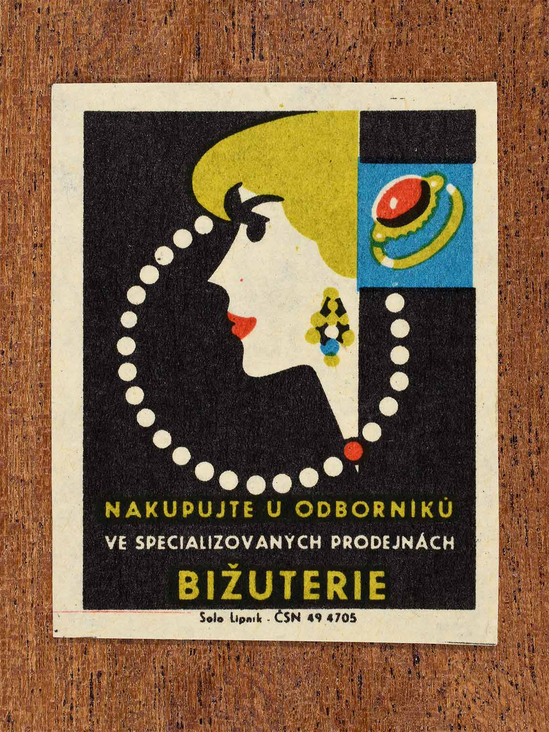 Vintage c. 1967 Czech matchbox label showing a woman wearing costume jewellery in black, yellow, red and blue colours. Produced by the Solo Lipník match factory to promote shopping for costume jewellery in specialised retail stores.