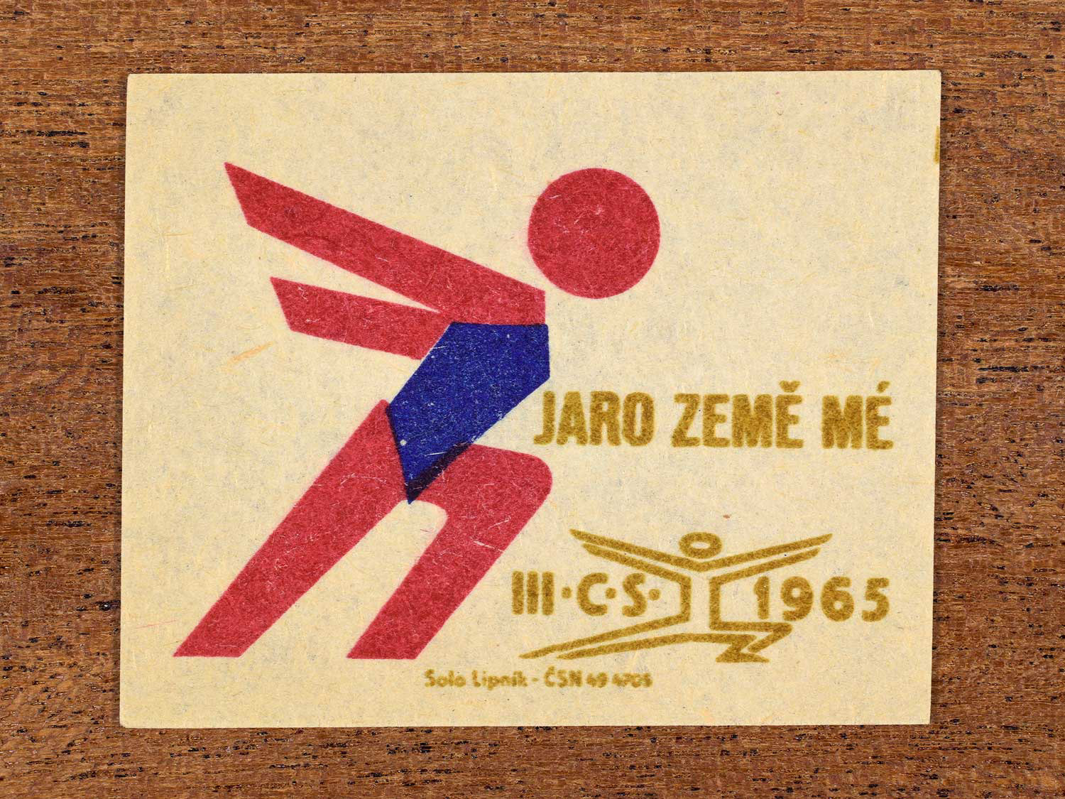 Vintage 1965 Czechoslovak matchbox label showing an abstract athlete figure, in blue, red and gold colours. Produced by the Solo Lipník match factory to promote physical fitness and sporting achievement.